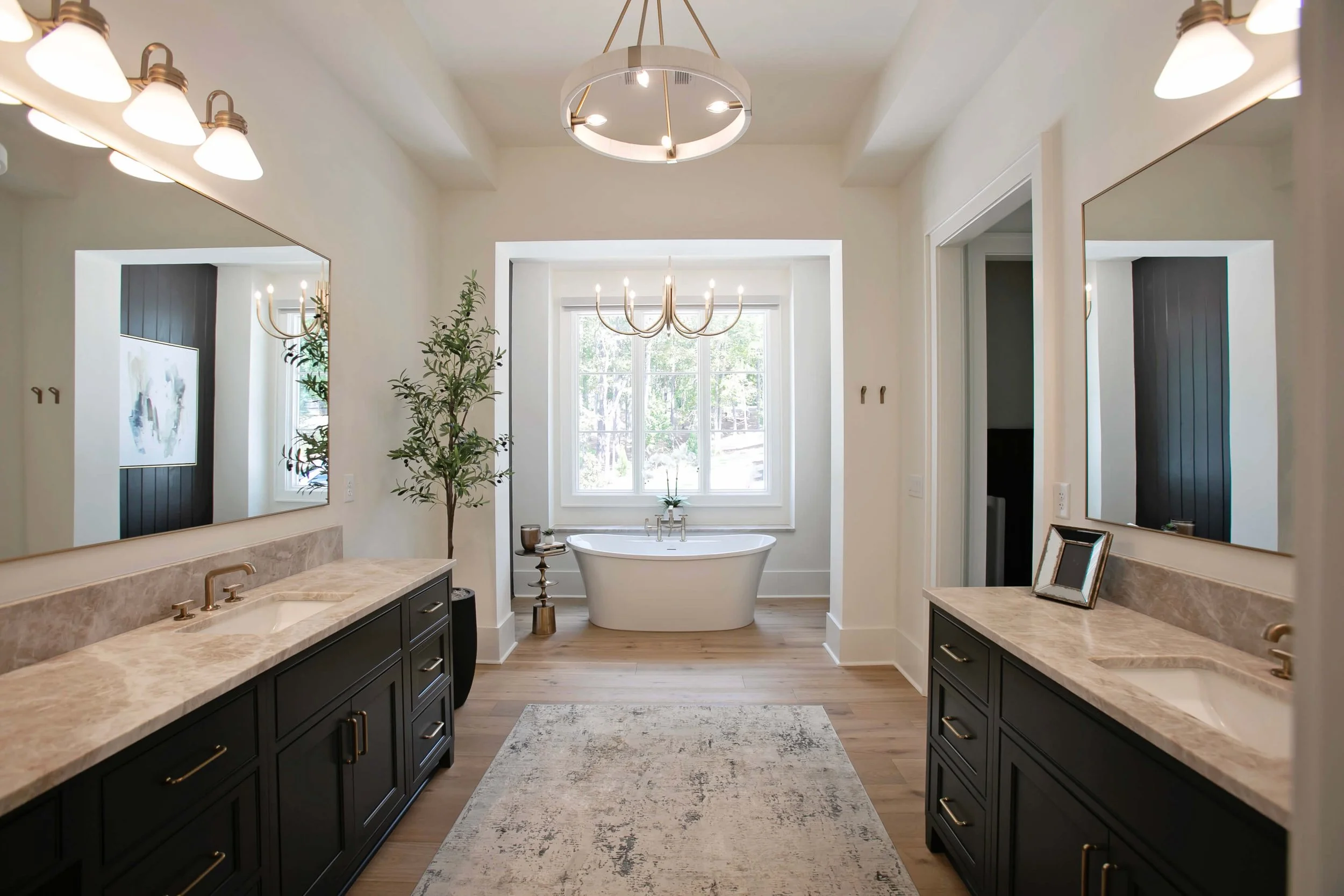 Luxury bathroom featuring custom dark cabinetry, dual vanities, marble countertops, modern lighting, and a freestanding tub in Greensboro, Georgia near Lake Oconee.