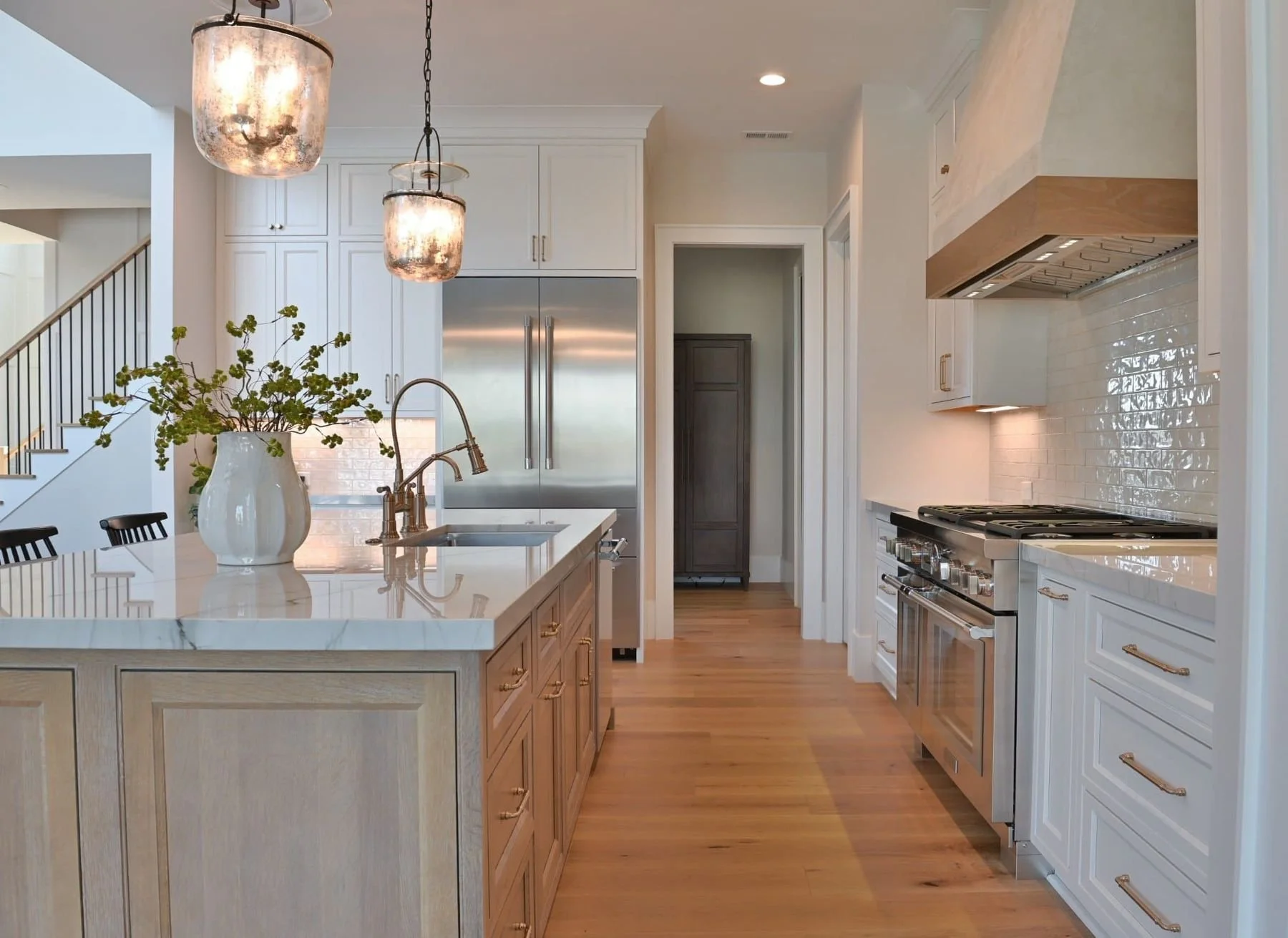 Custom kitchen cabinetry and hardwood flooring in a luxury Lake Oconee home in Greensboro, Georgia. The kitchen features warm wood cabinets, a large center island with integrated storage, white subway tile backsplash and floating wood shelves