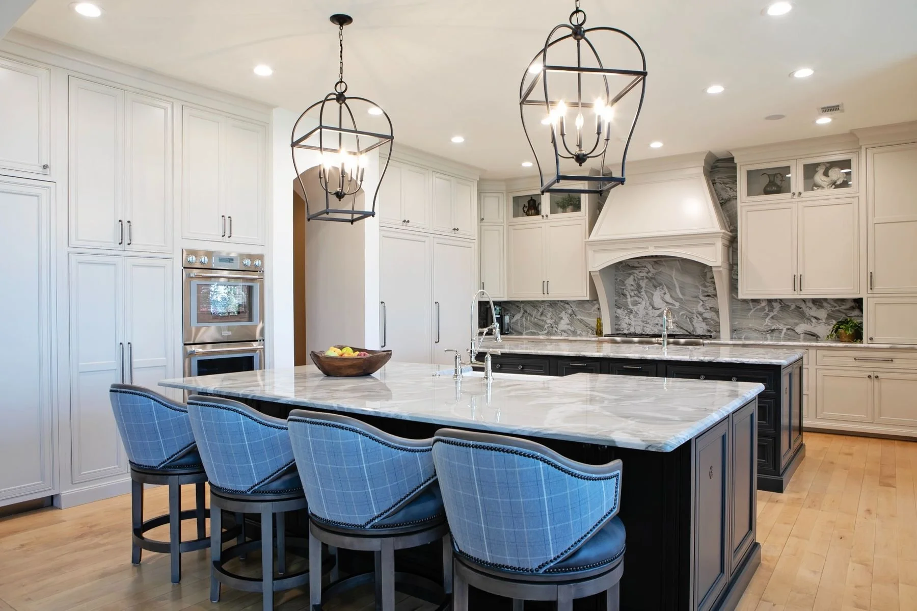 Custom kitchen cabinetry and hardwood flooring in a luxury Reynolds Lake Oconee home in Greensboro, Georgia. The kitchen features painted white perimeter cabinets, a contrasting dark island, marble countertops, decorative pendant lighting, and light 