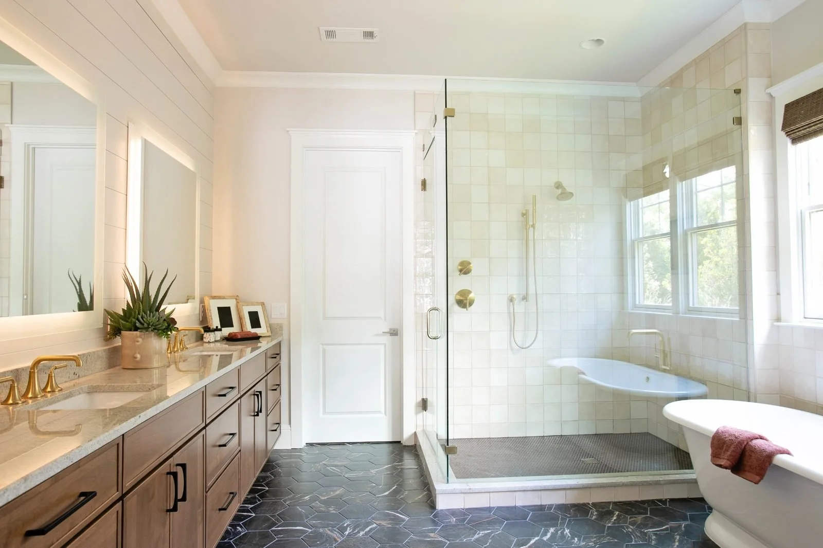 Custom bathroom cabinetry and tile flooring in a luxury Reynolds Lake Oconee home in Greensboro, Georgia. The bathroom features a warm wood double vanity with quartz countertops, a frameless glass shower, freestanding soaking tub & large-format tile