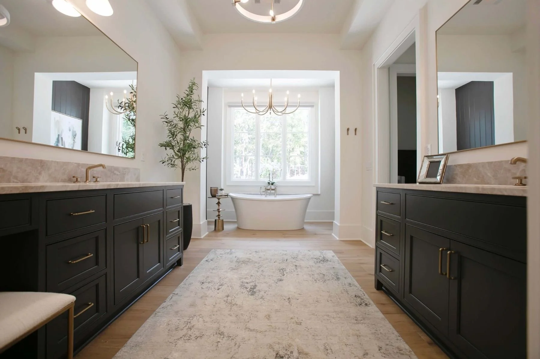 Custom bathroom cabinetry and luxury flooring in a Reynolds Lake Oconee home in Greensboro, Georgia. The spacious primary bathroom features dark painted double vanities with abundant storage, quartz countertops, a large soaking tub, and elegant floor