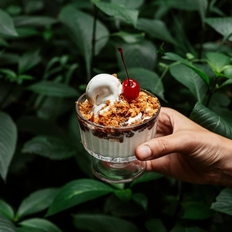pessoa segurando uma taça de sorvete sundae, com uma cereja em calda por cima, no Futuro Refeitório