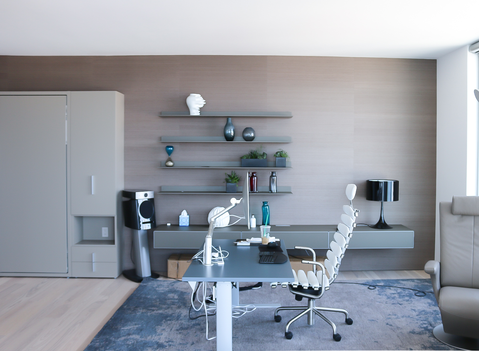 Taupe murphy bed, floating cabinet, glass desk table and a leather office chair.