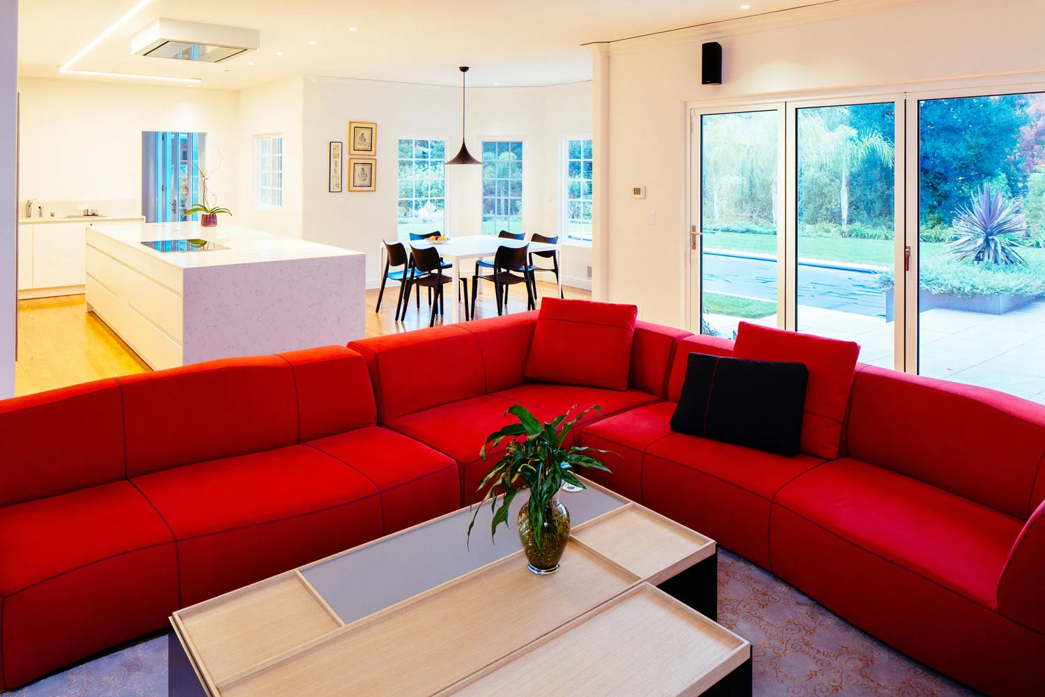 The den features a bright red sectional sofa creating a contrast with the white kitchen.