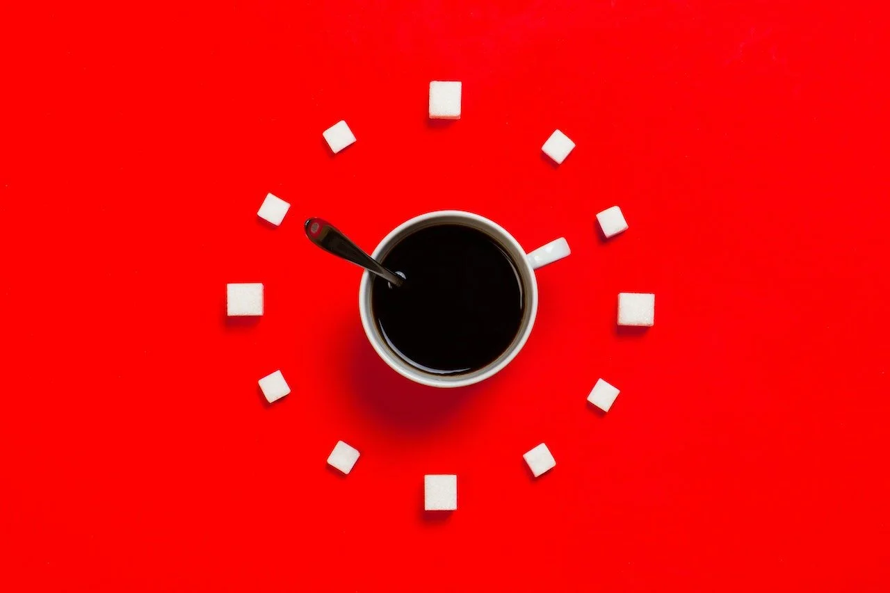 clock made out of sugar lumps and mug of coffee with spoon on red background