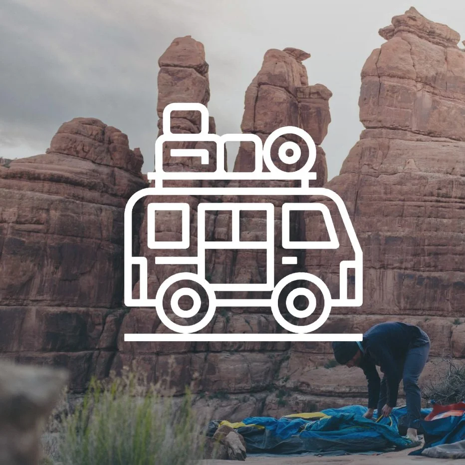 A person setting up camping equipment near red rock formations in a desert landscape.