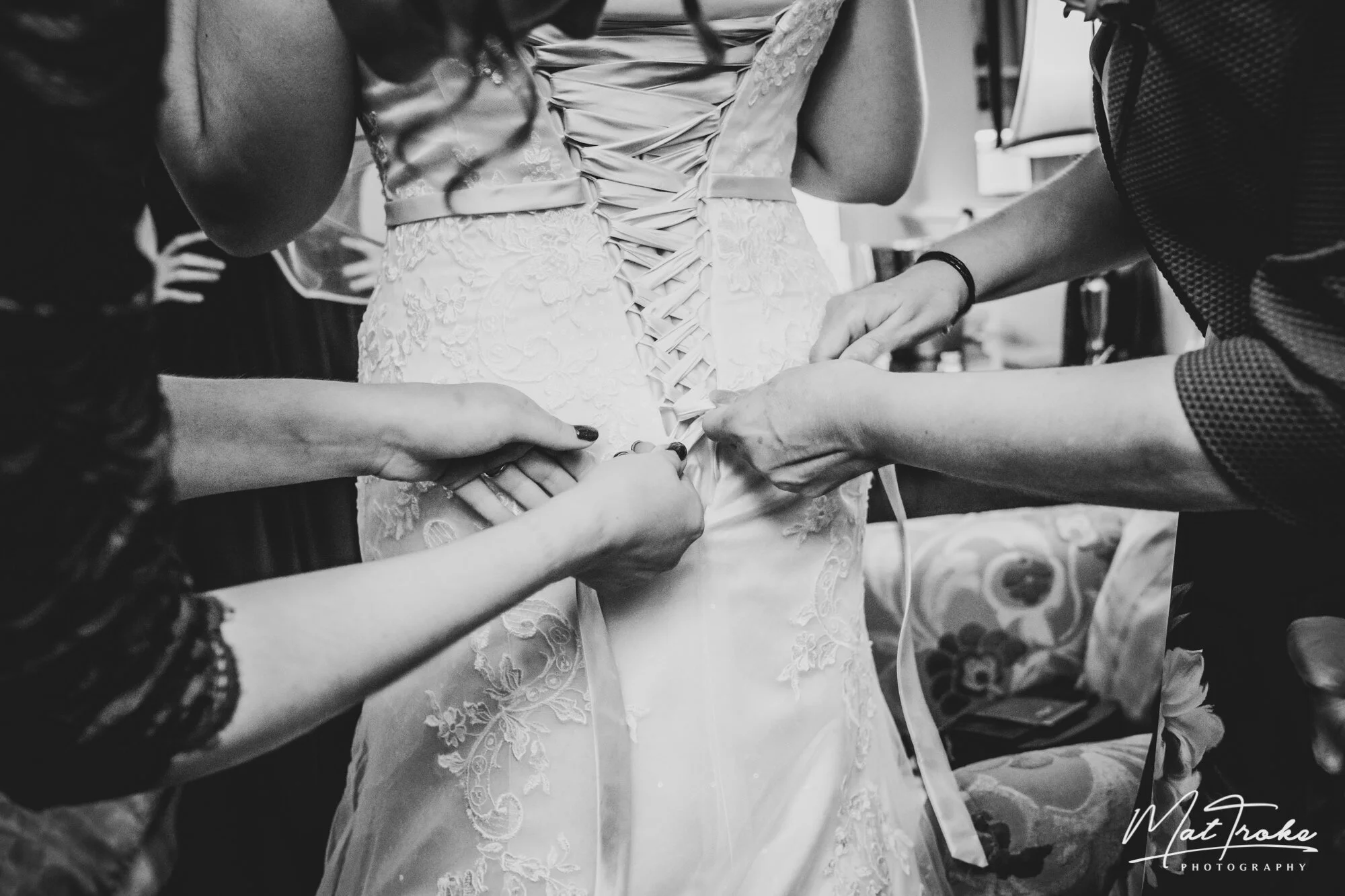 Mother fastening the brides dress ribbon with mother and bridesmaids before ceremony