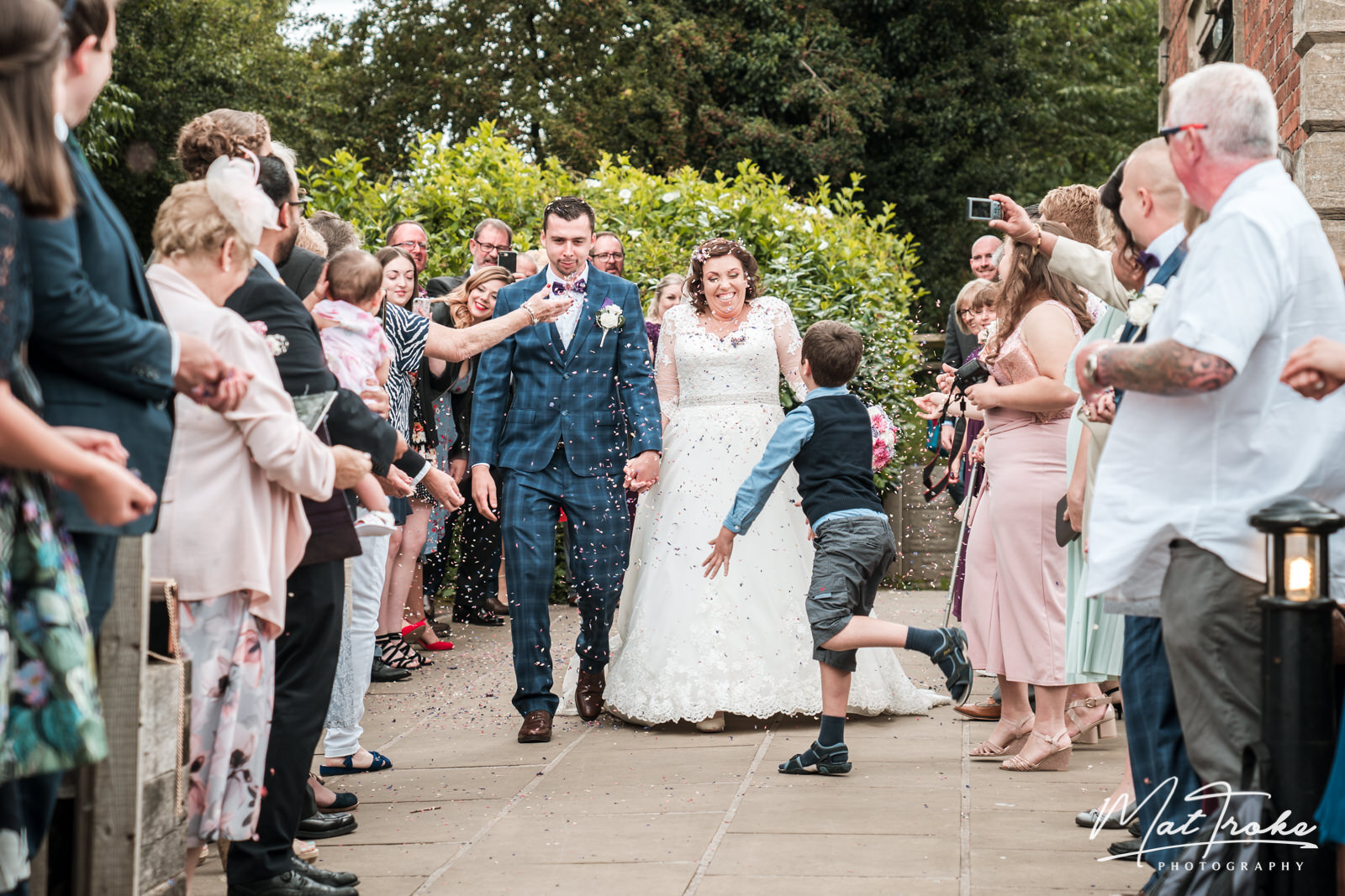 Confetti throw throwing at bride and groom by page boy and wedding guests just married