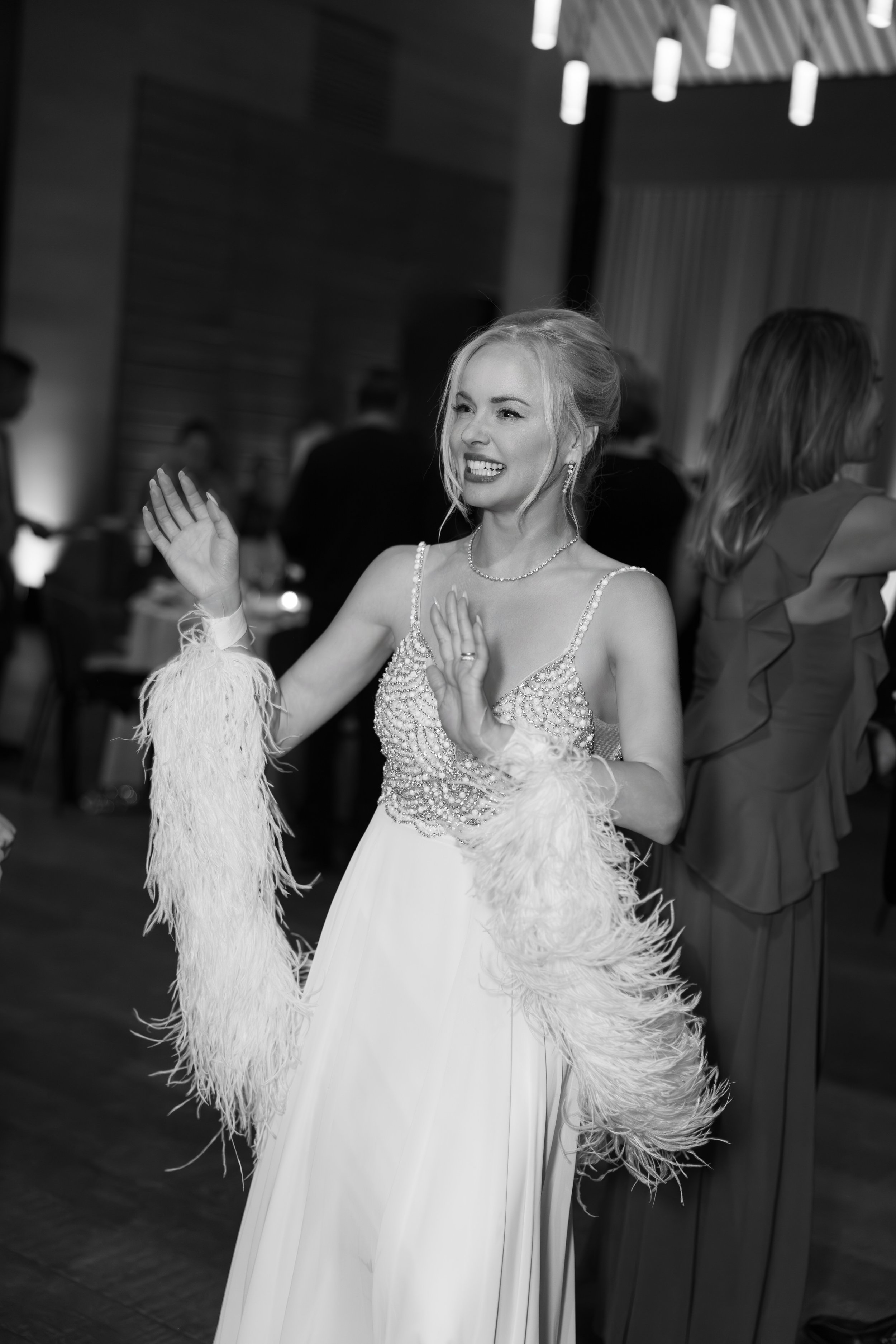 A woman in a glamorous dress with feathered sleeves dancing at a celebration or party.