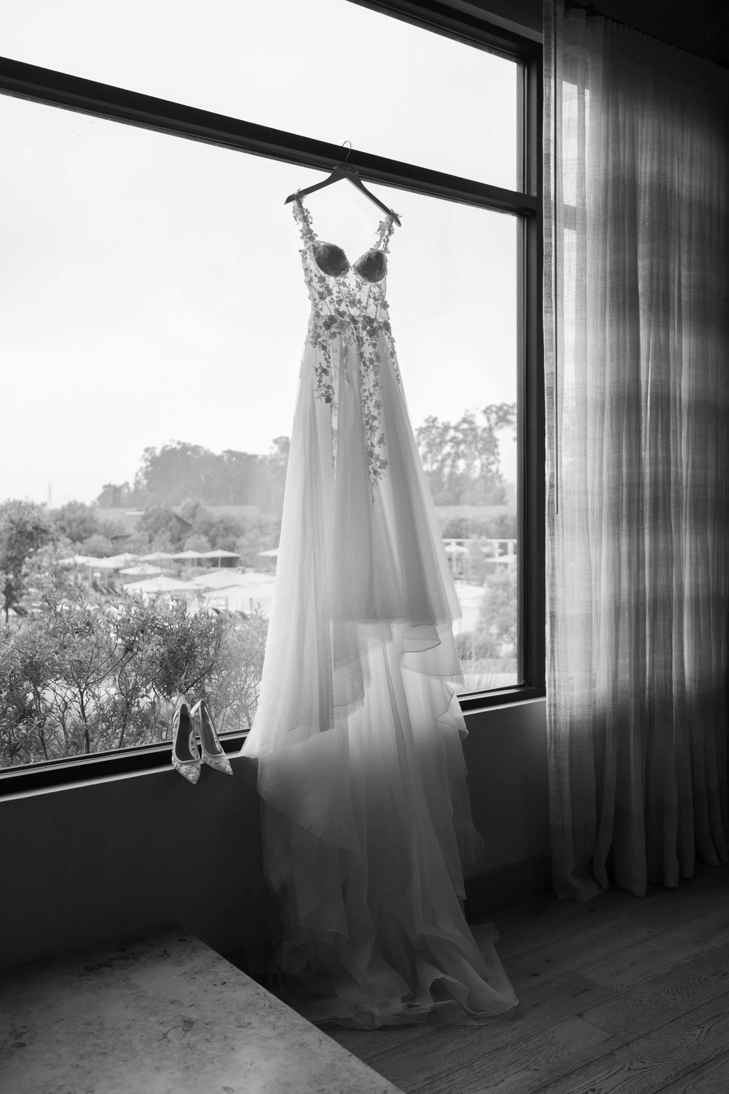 Wedding dress and high heels hanging by a window.