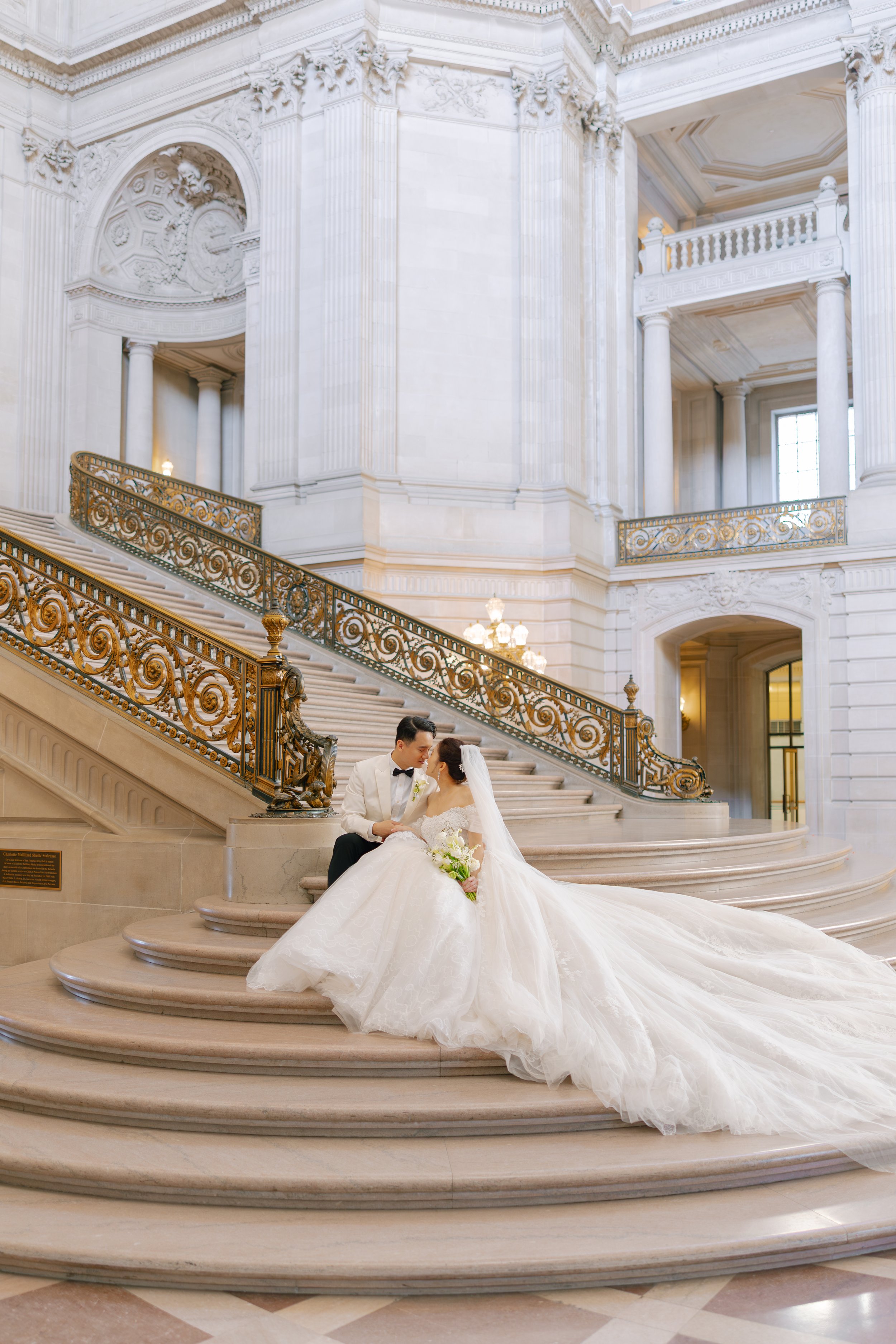 Close-up of a cascading wedding bouquet featuring white and soft pink orchids, with a lace wedding dress partially visible in the background.