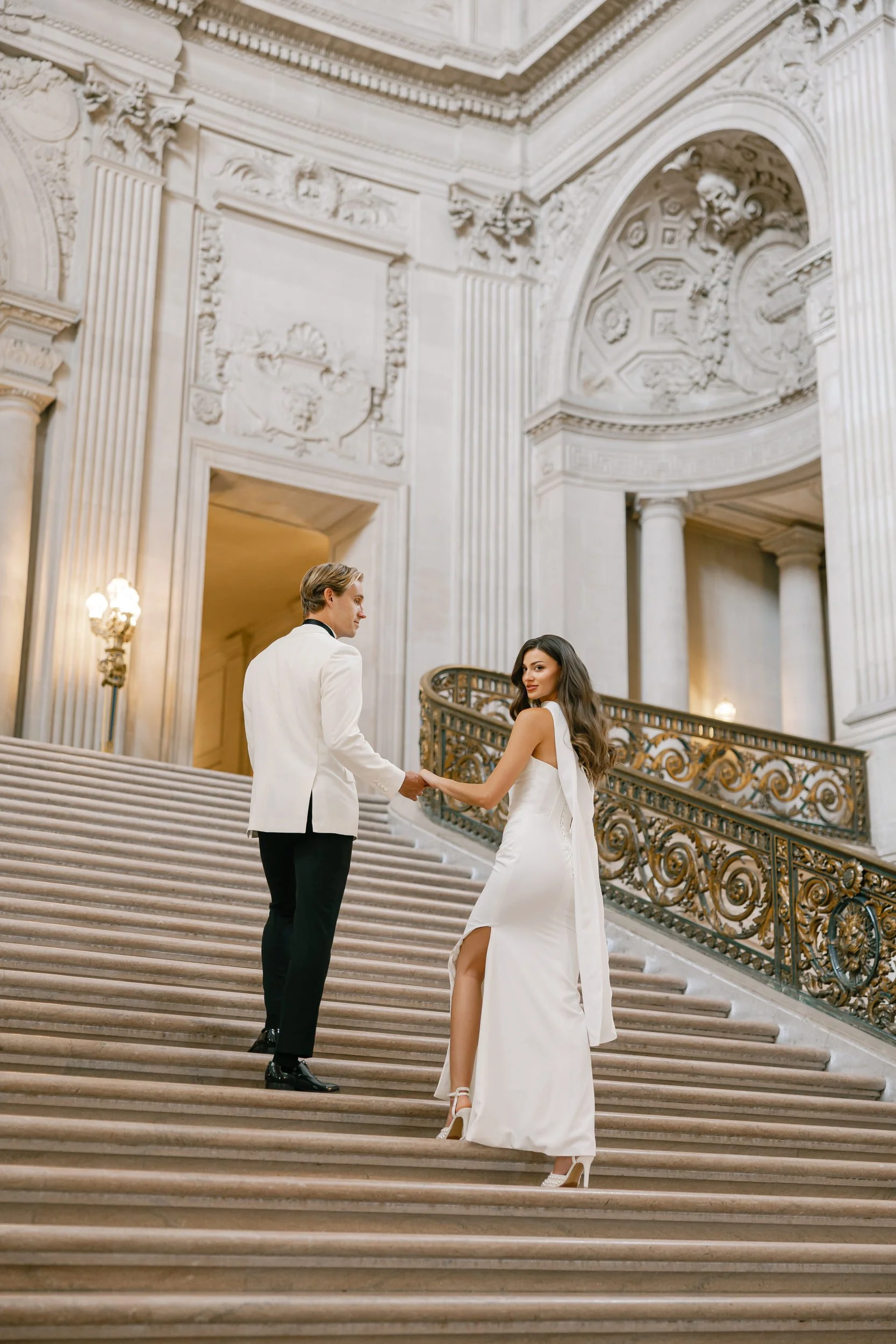 Elegant couple holding hands on the staircase inside San Francisco City Hall during their intimate wedding ceremony.