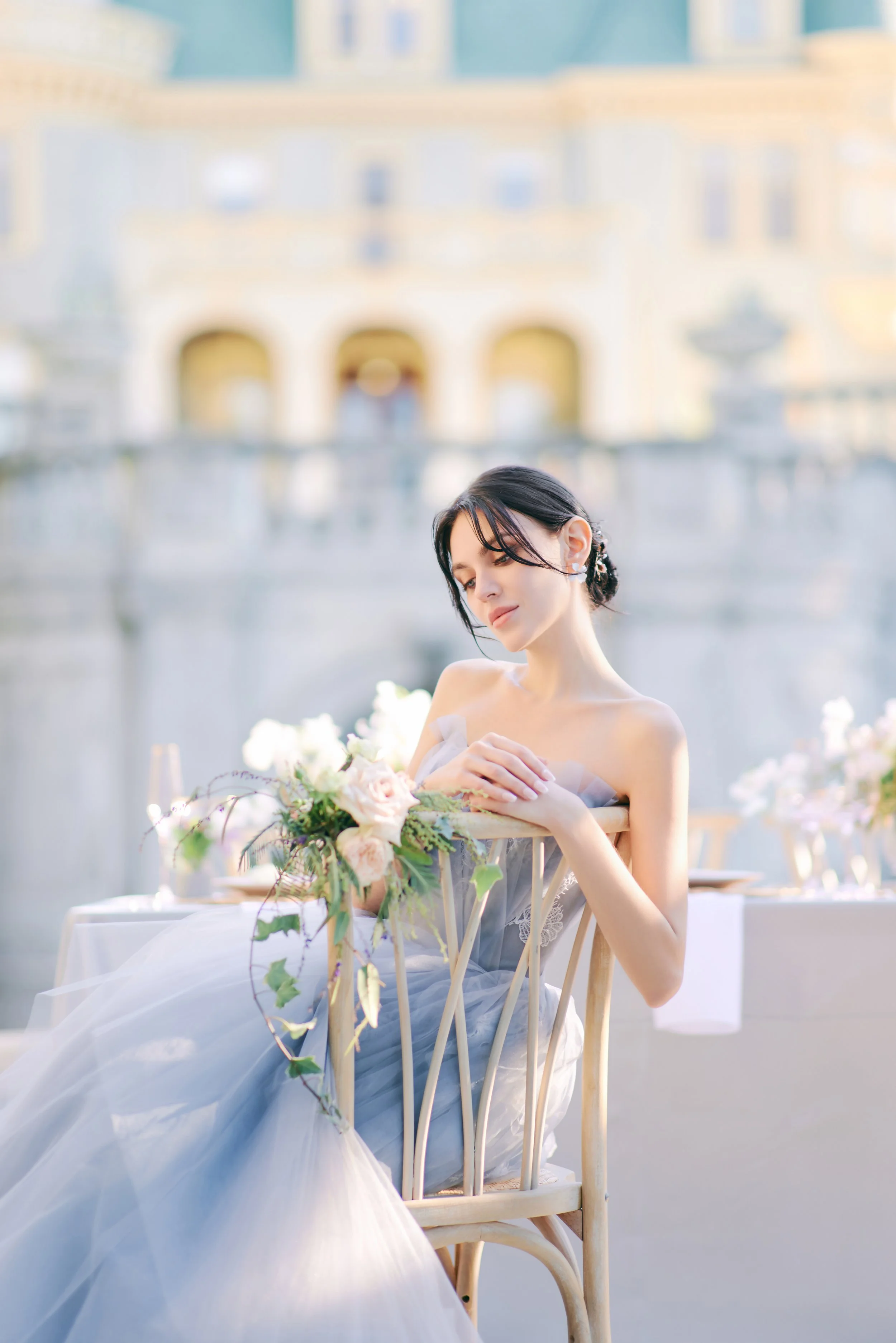 Elegant outdoor table setting with white floral centerpiece, wine glasses filled with white wine, a carved white bust statue, and fine china, suggesting a wedding or celebration.