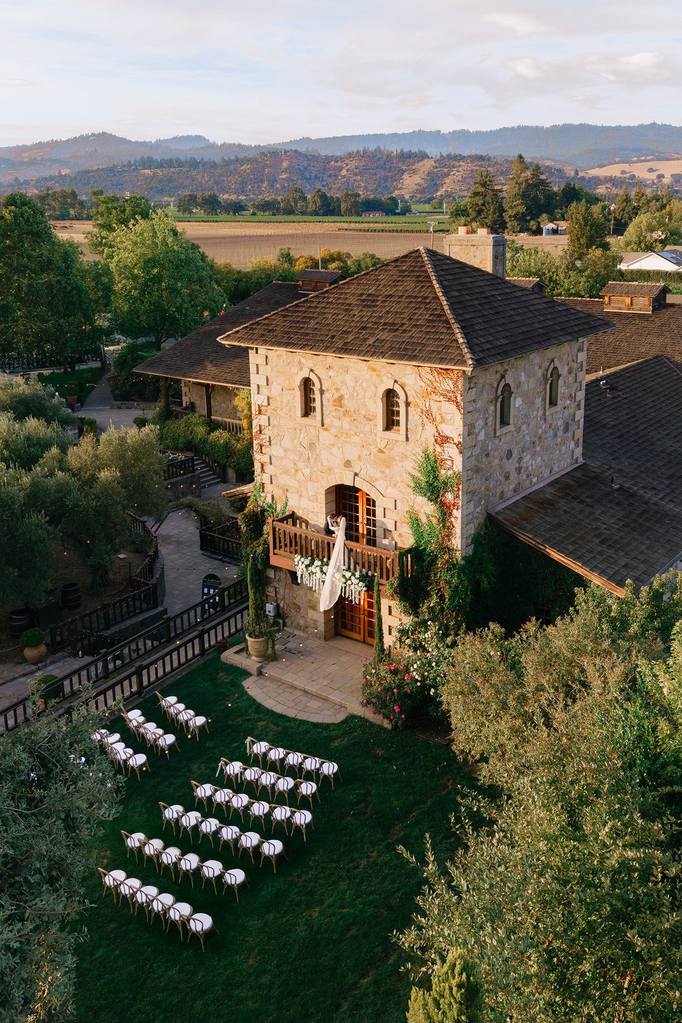 Aerial view of an elegant outdoor wedding ceremony at a Napa Valley winery surrounded by vineyards and olive trees.
