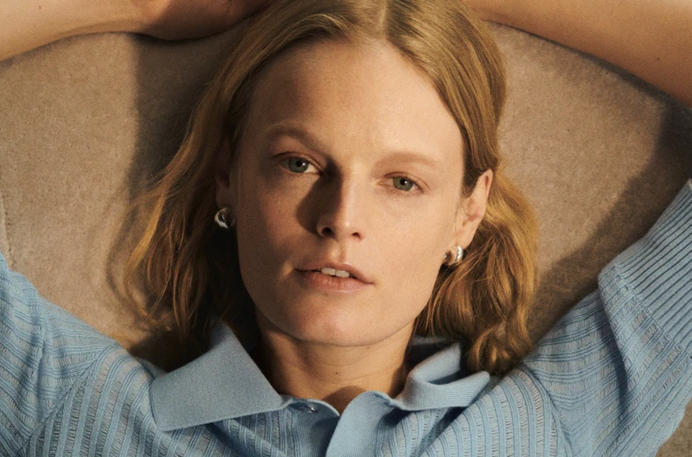 Blonde woman relaxes with arm's behind her head after doing her five minute makeup routine that makes her look instantly polished