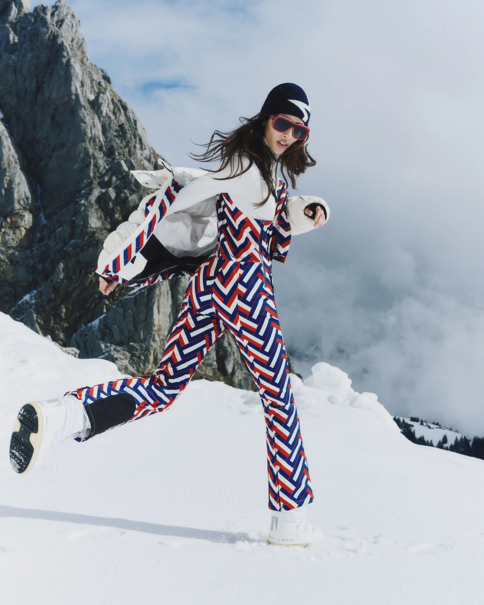 Female model runs in the snow across snowy mountains wearing Perfect Moment skiwear