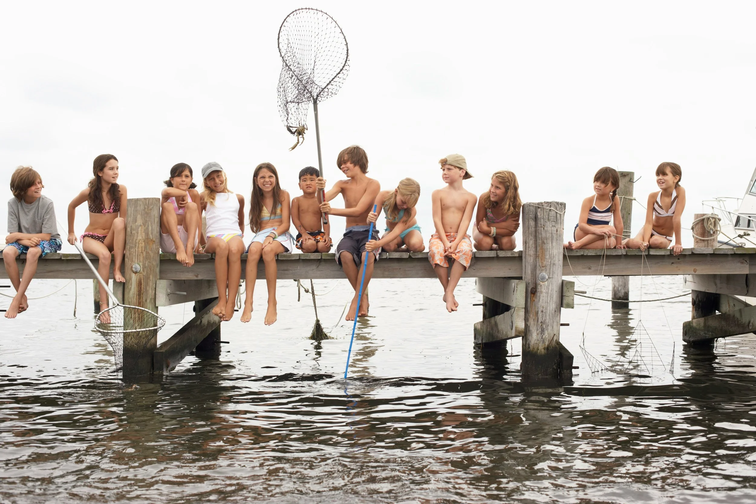 Children spending an unstructured summer afternoon together on a wooden jetty, fishing, chatting and entertaining themselves outdoors