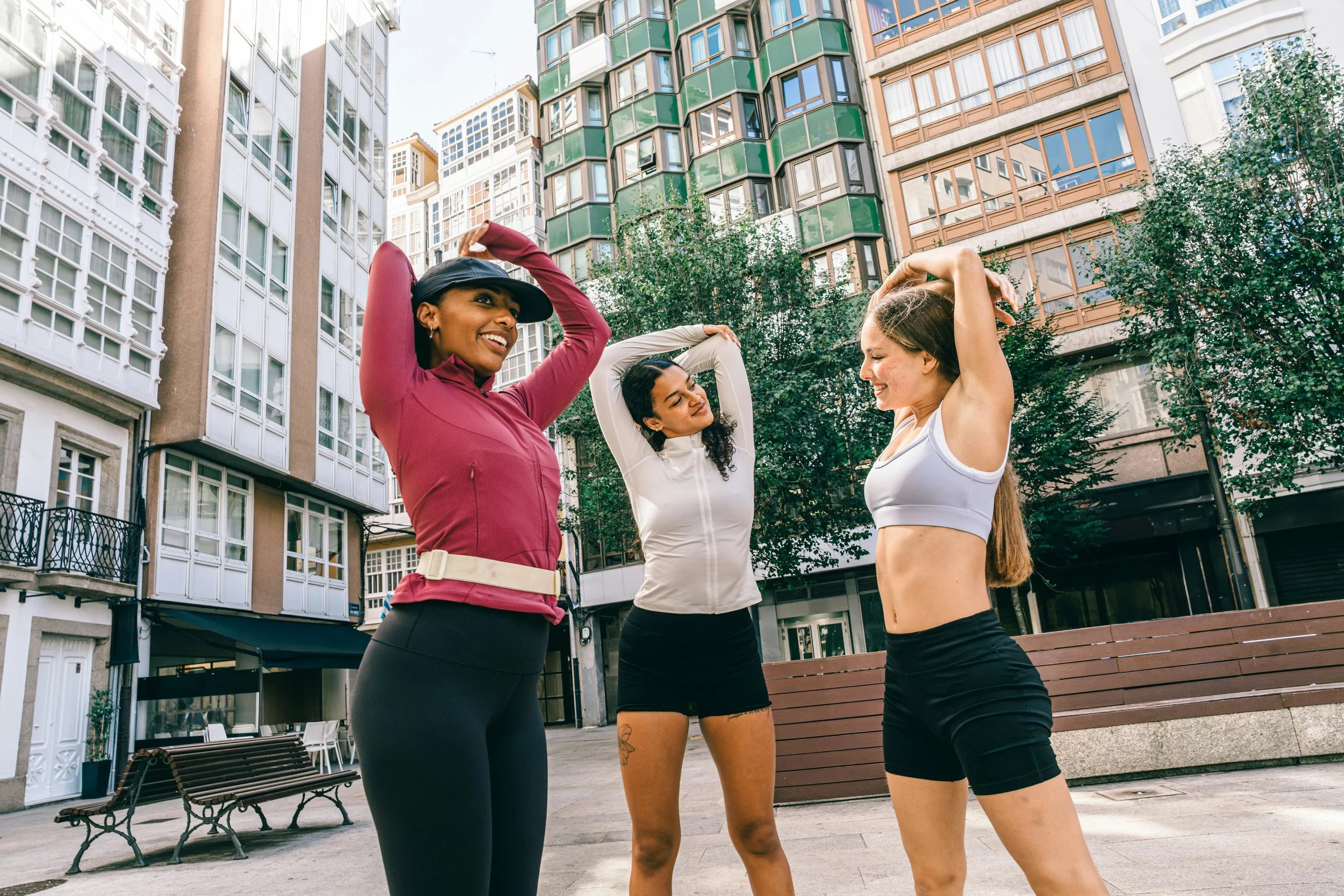 Three women stretching together after a workout in an urban setting, highlighting exercise, recovery and stress management.