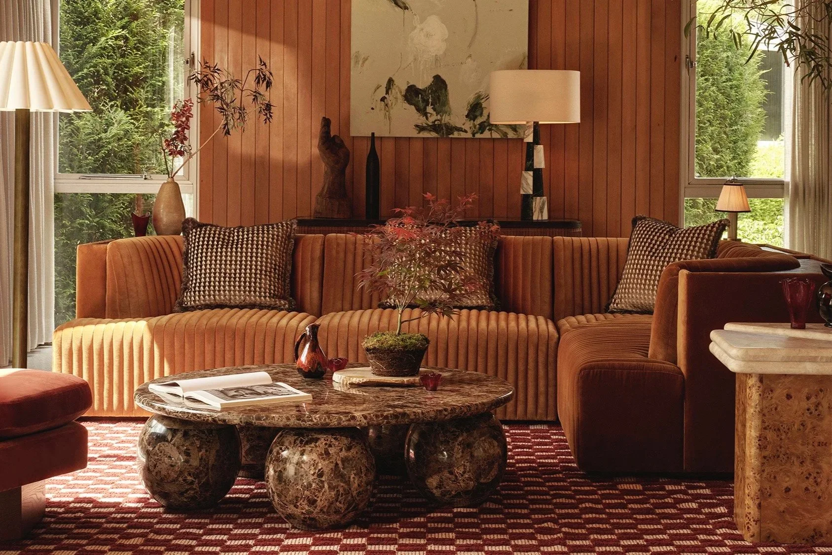Warm 90s-inspired living room by Soho Home with curved sofa, wood panelling, marble coffee table and soft ambient lighting
