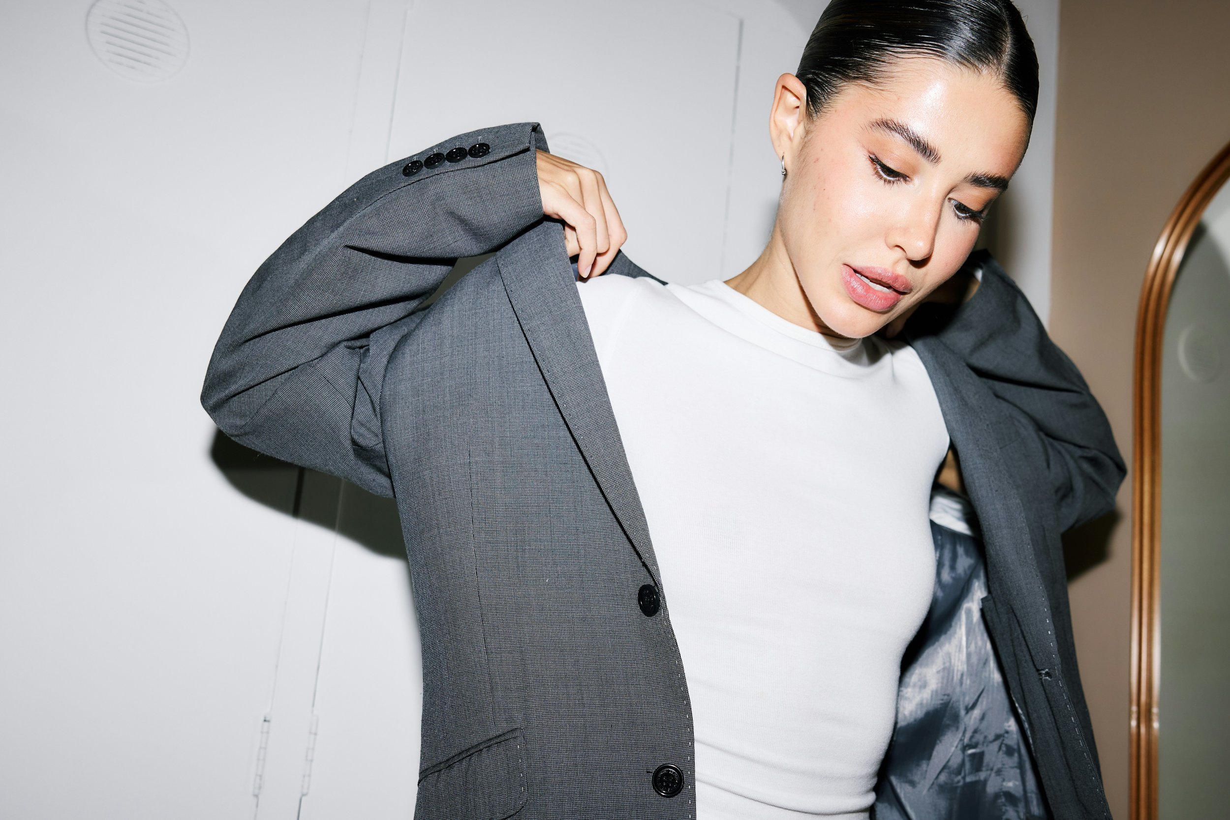 putting on jacket to leave the house, after standing in front of the mirror adjusting waist band, illustrating water retention and body fluctuation — Editors Beauty