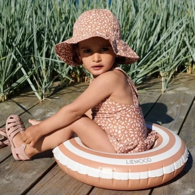 Girl puts shoes on while wearing Liewood sun hut