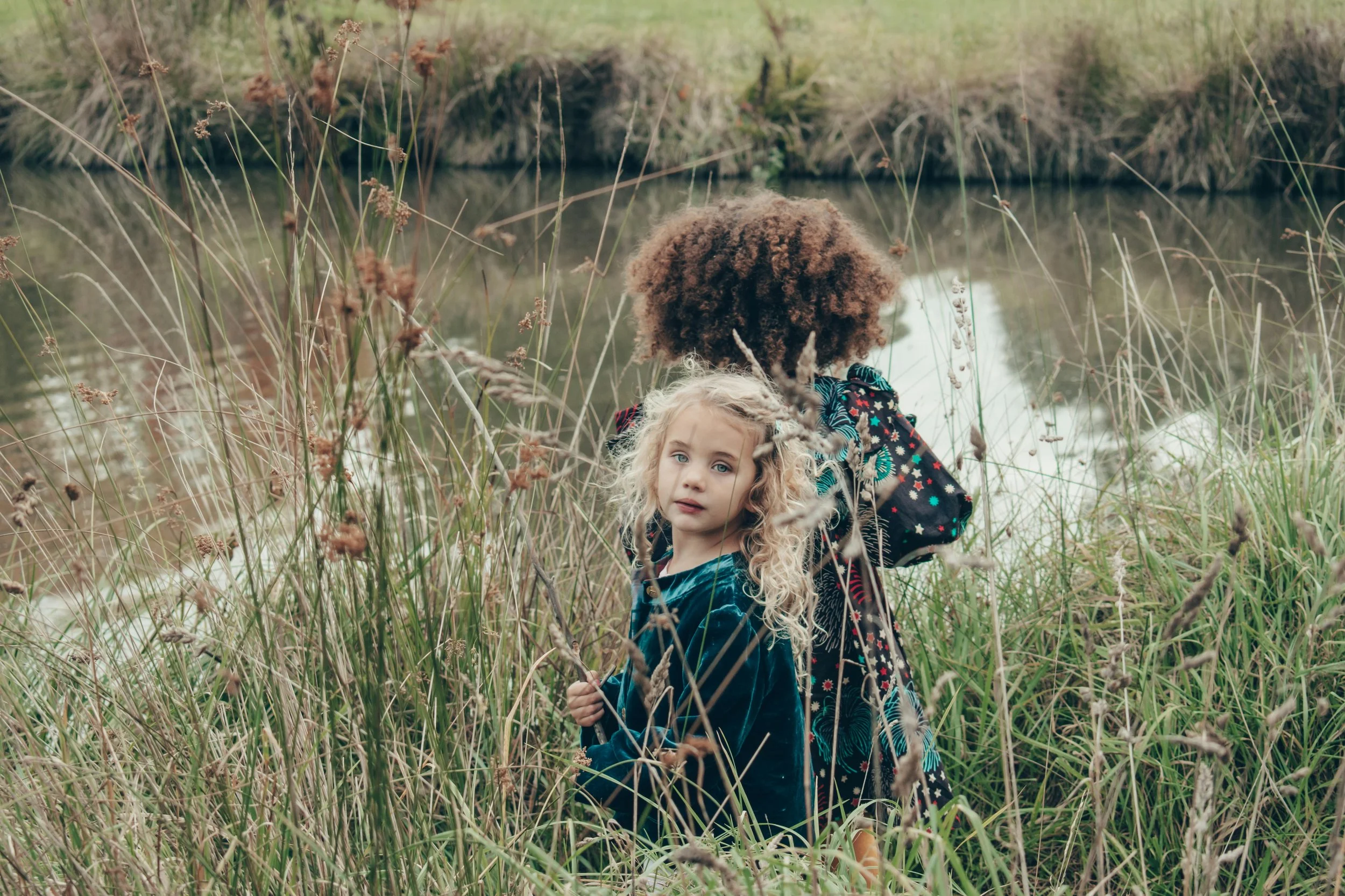 Two preschool-age girls playing together in long grass outdoors