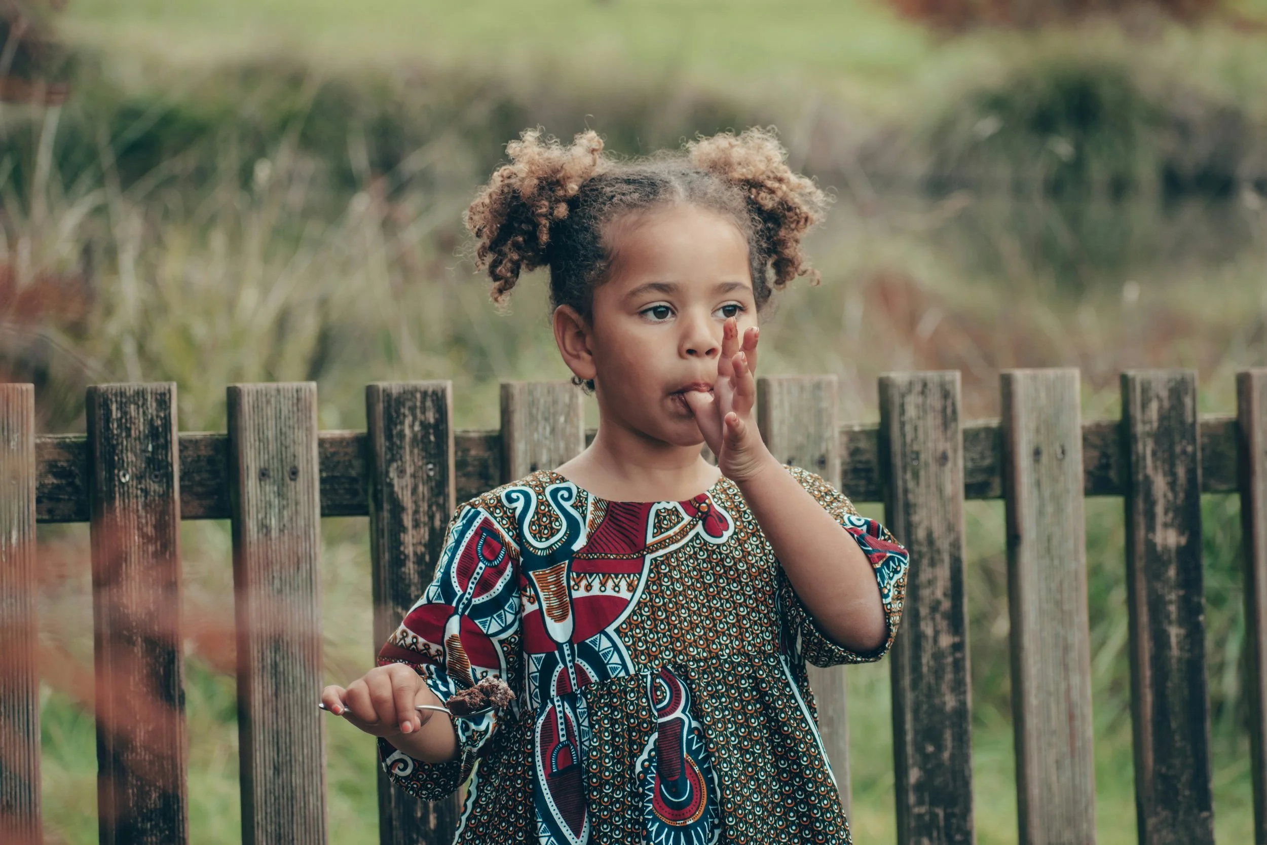 Young girl talking outdoors beside a wooden fence