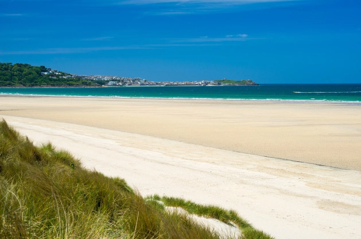 Porthkidney Beach in Cornwall with wide sandy shoreline, turquoise sea and views towards St Ives Bay.