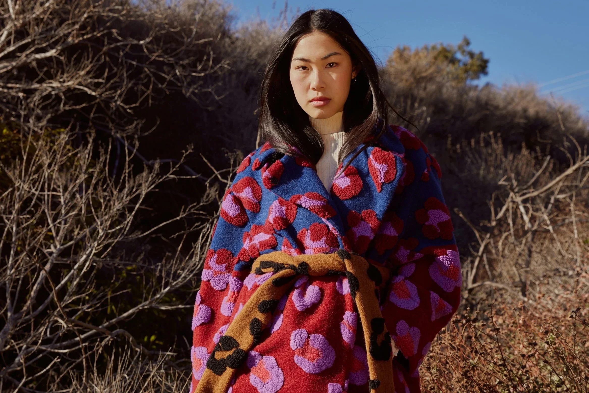 Woman in bright orange jacket outdoors in soft spring light representing seasonal skin renewal