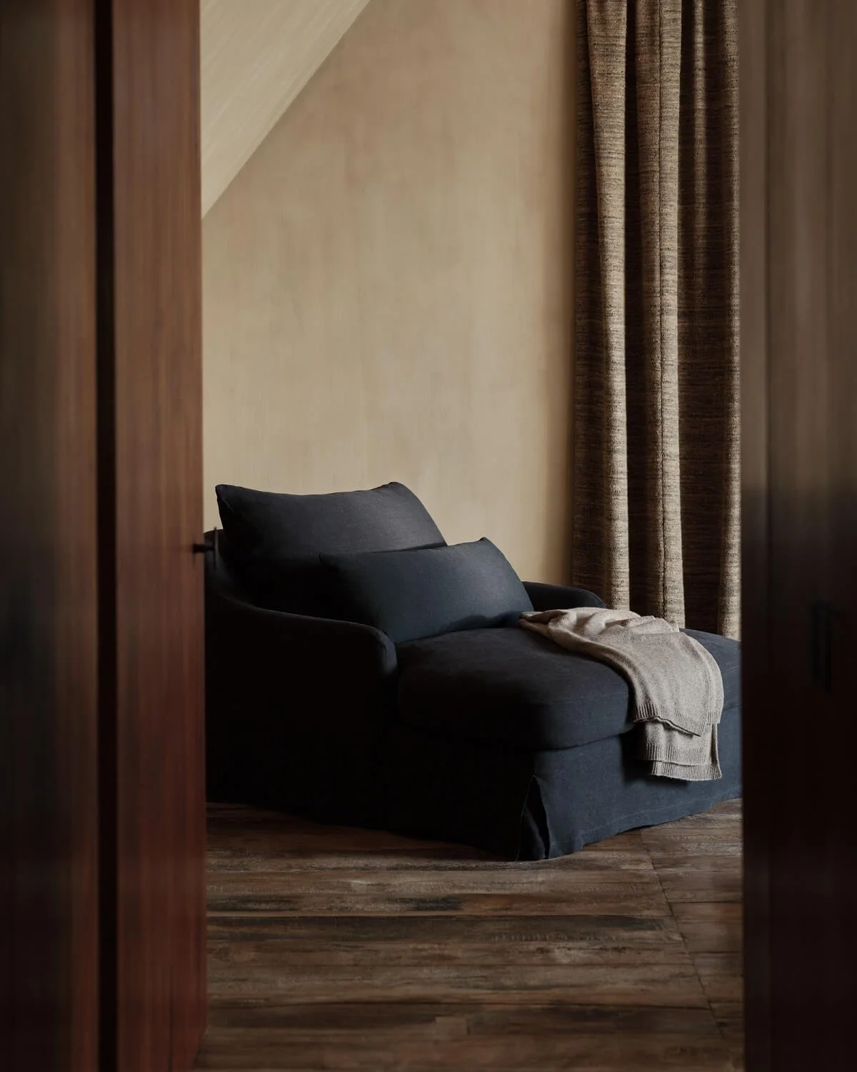 View through door of room with plastered walls, wood floor and navy linen armchair - by Zara Home