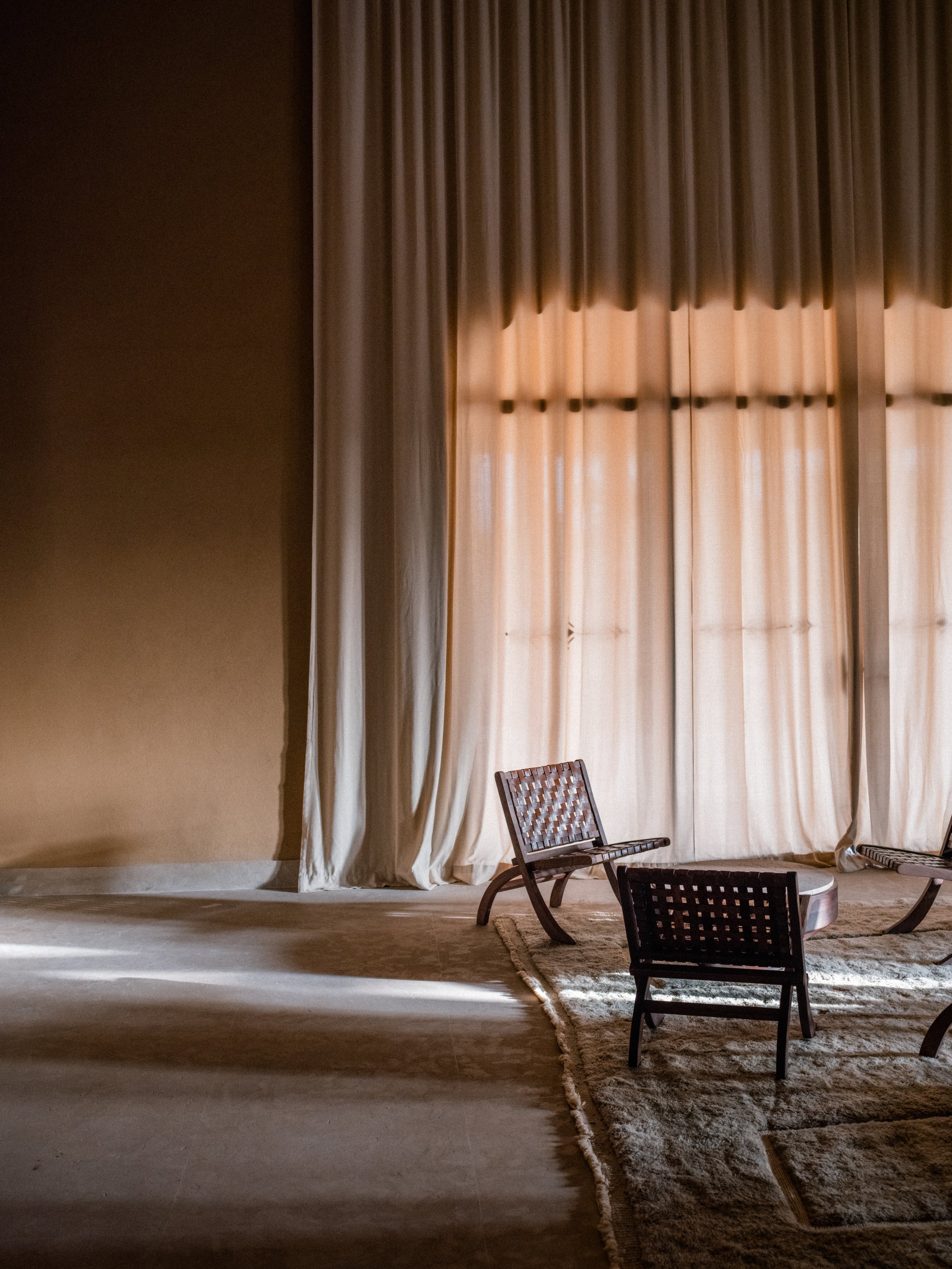 Minimalist lounge with woven wooden chairs, sheer curtains and natural textures at Oasis Lodges Marrakech