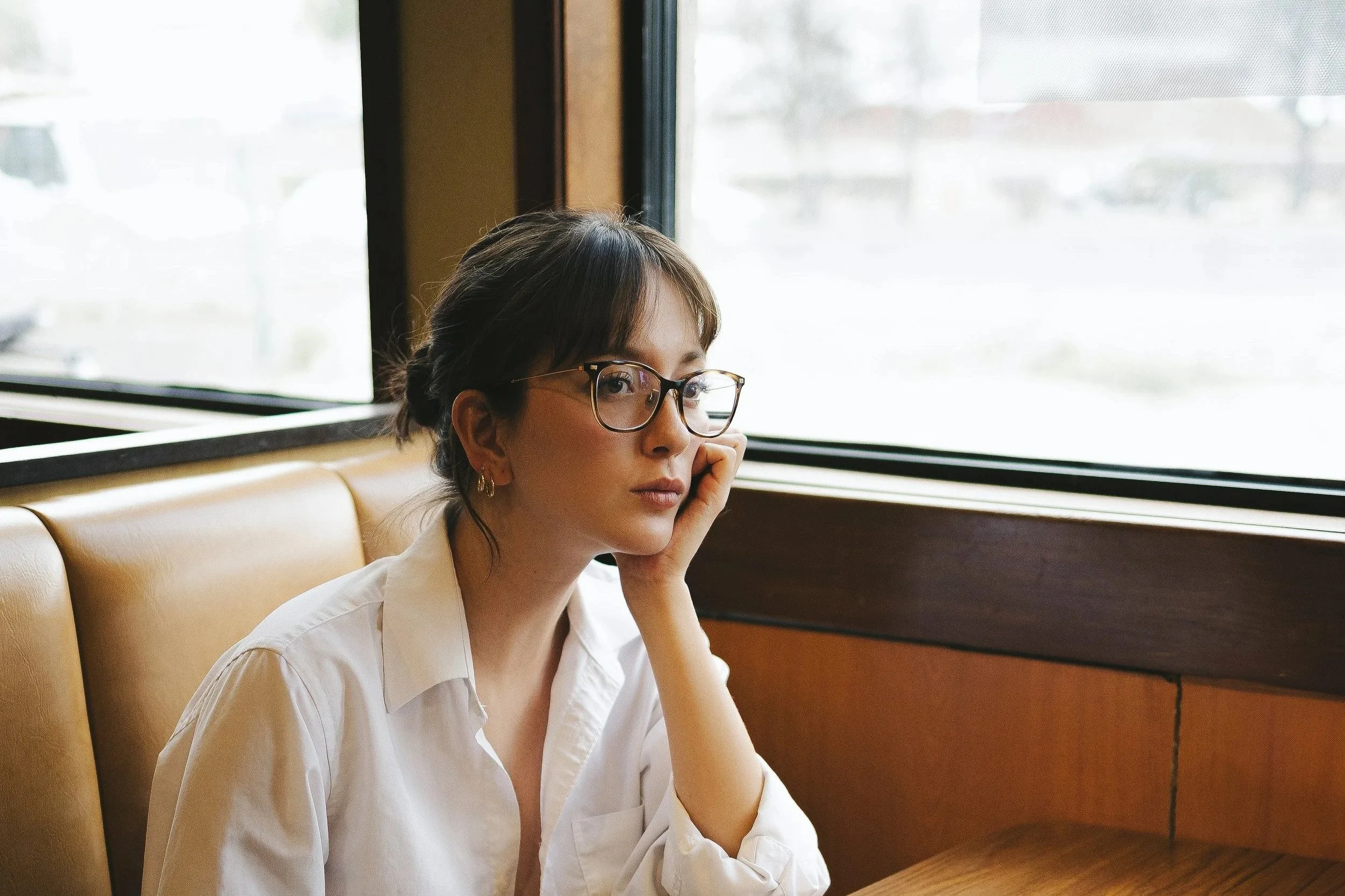 Woman with natural skin sitting by a window in soft daylight, illustrating calm, balanced complexion and minimal makeup.