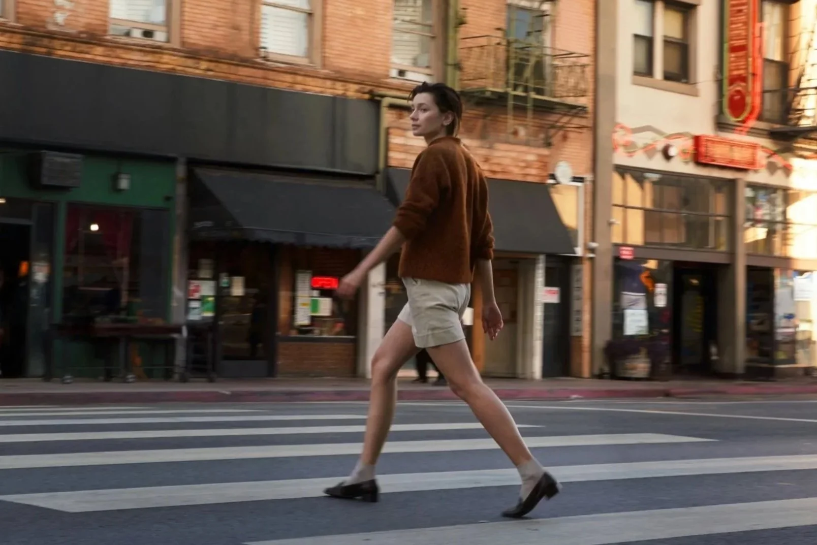 Woman walking across a city street in smart casual outfit combining knitwear and tailored shorts