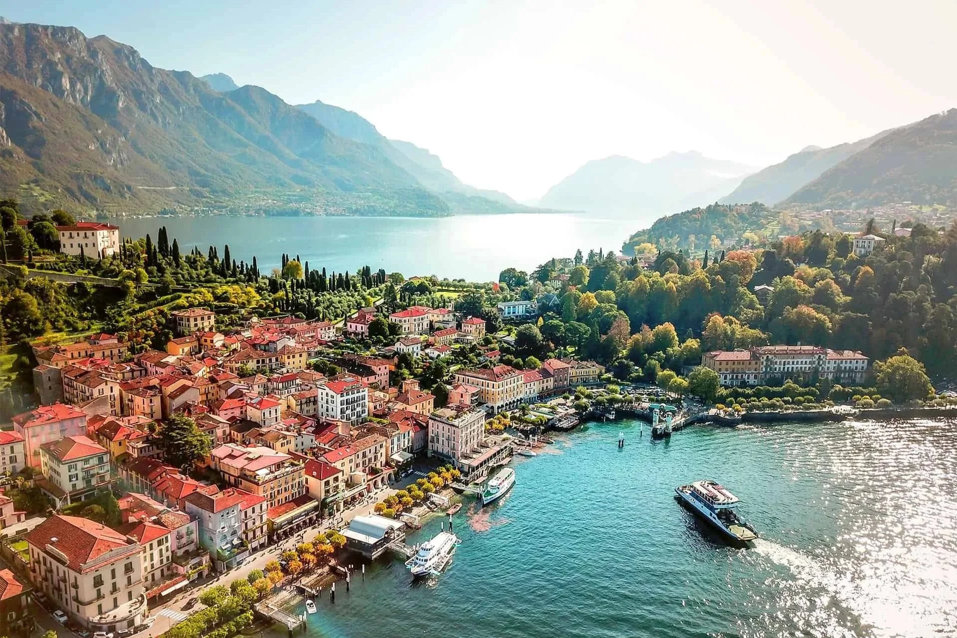 Aerial view of a lakeside village on Lake Como with terracotta rooftops, boats and surrounding mountains