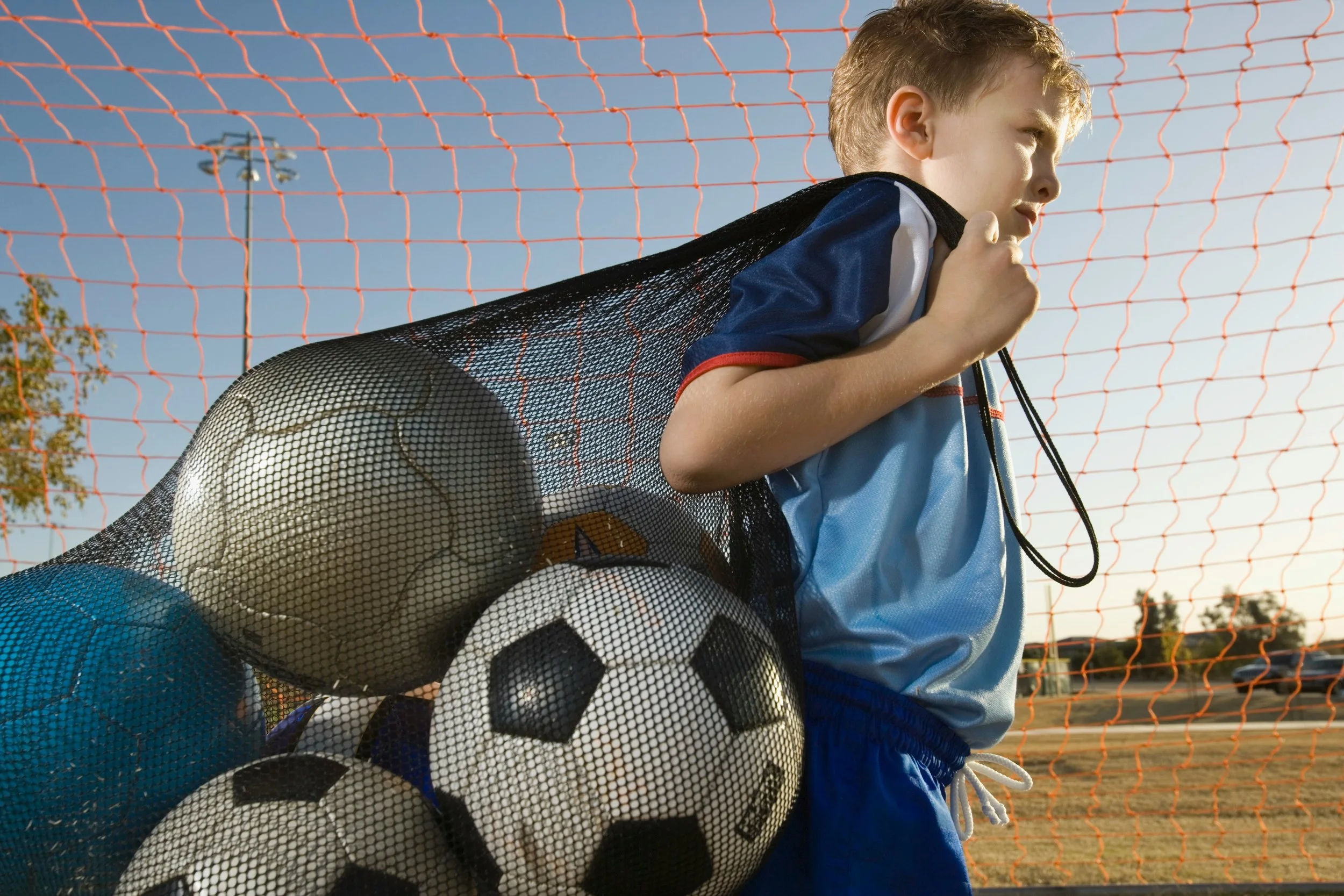 Young football player carrying a bag of footballs after training, highlighting the practice involved in developing sporting skills.