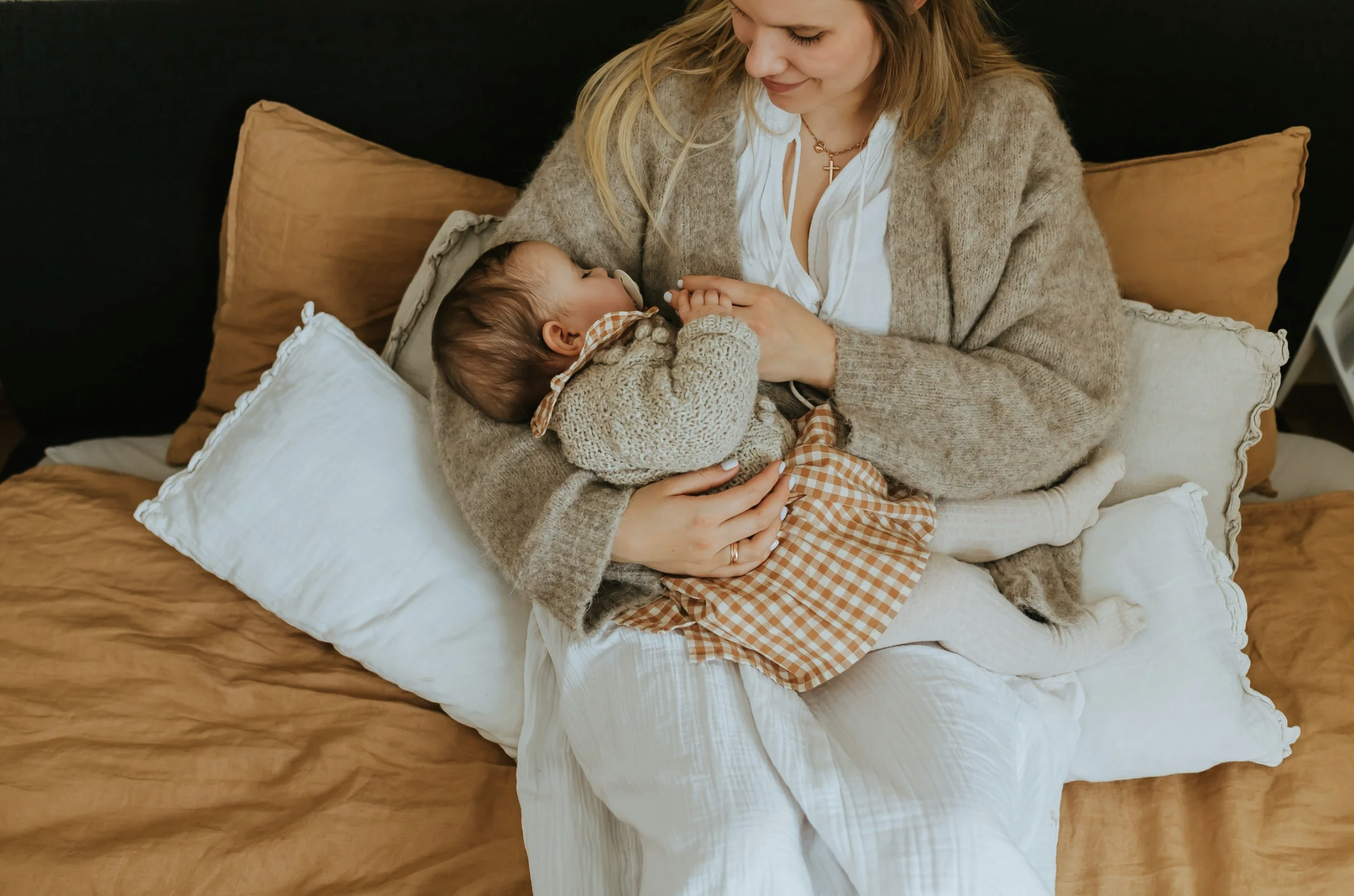 Mother holding a baby close on a bed, soft natural light, calm and reassuring photography.