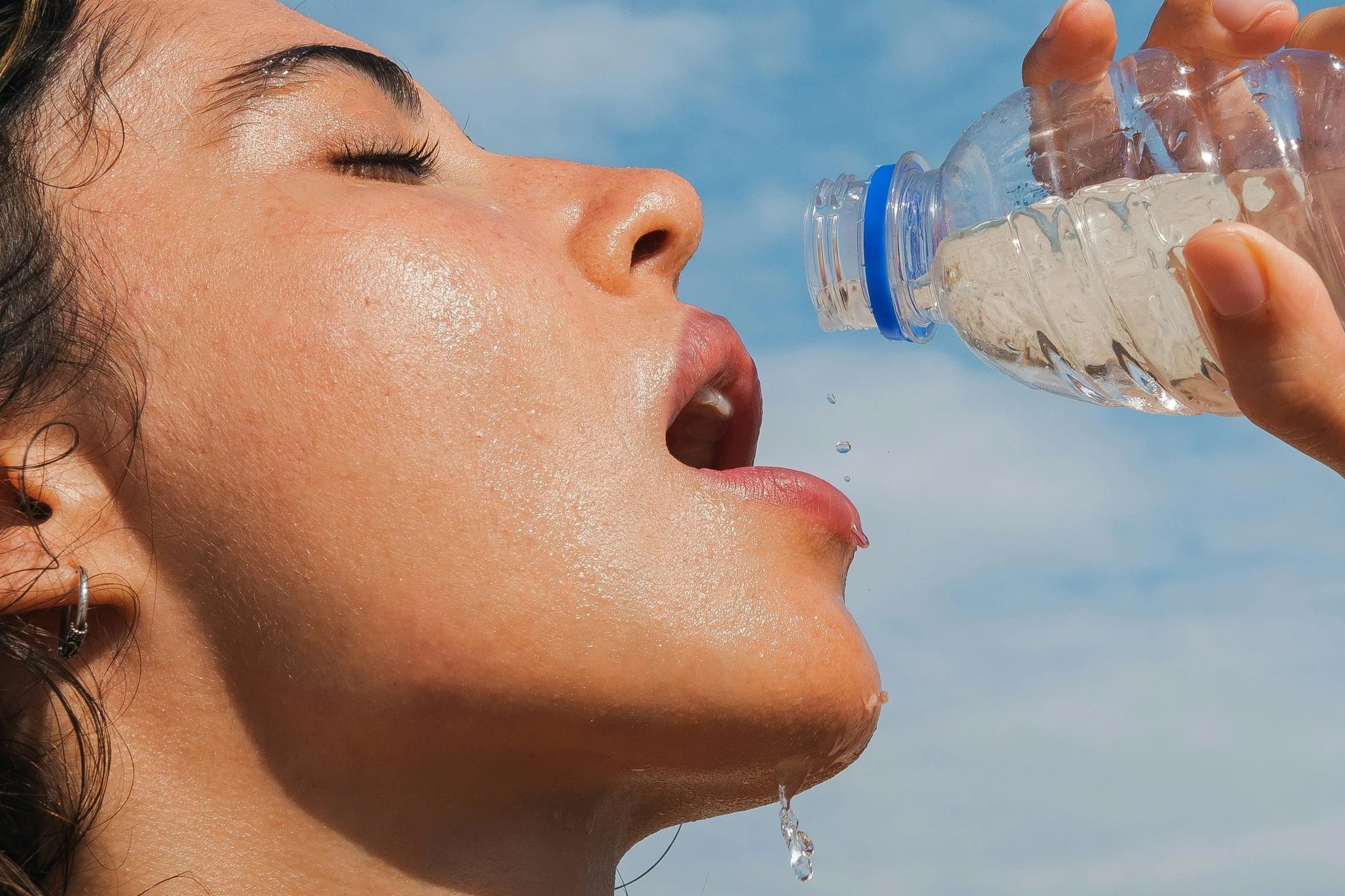 Woman drinking water from a bottle in sunlight, close-up hydration and glowing skin texture