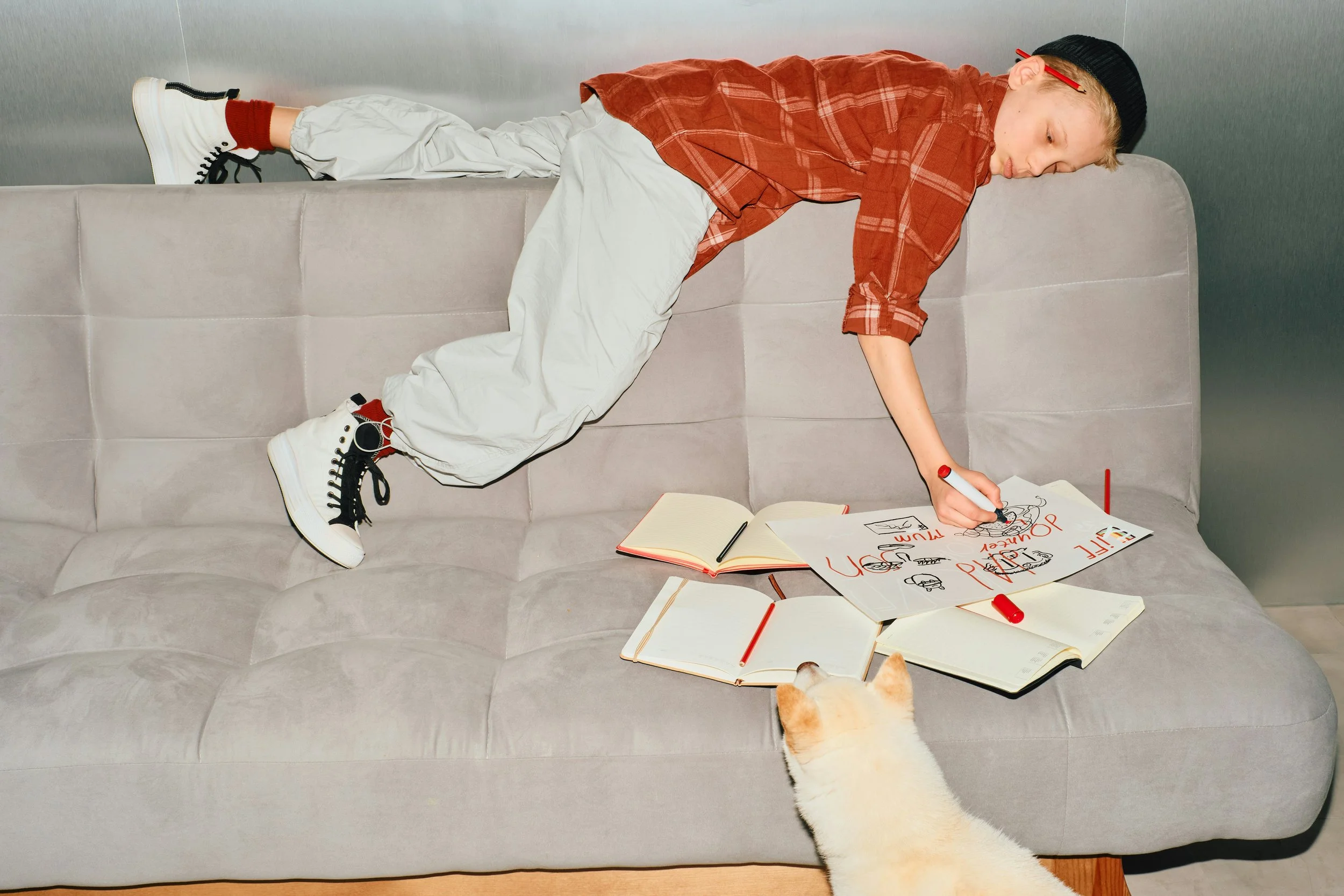 Boy lying across a sofa surrounded by school books and notebooks