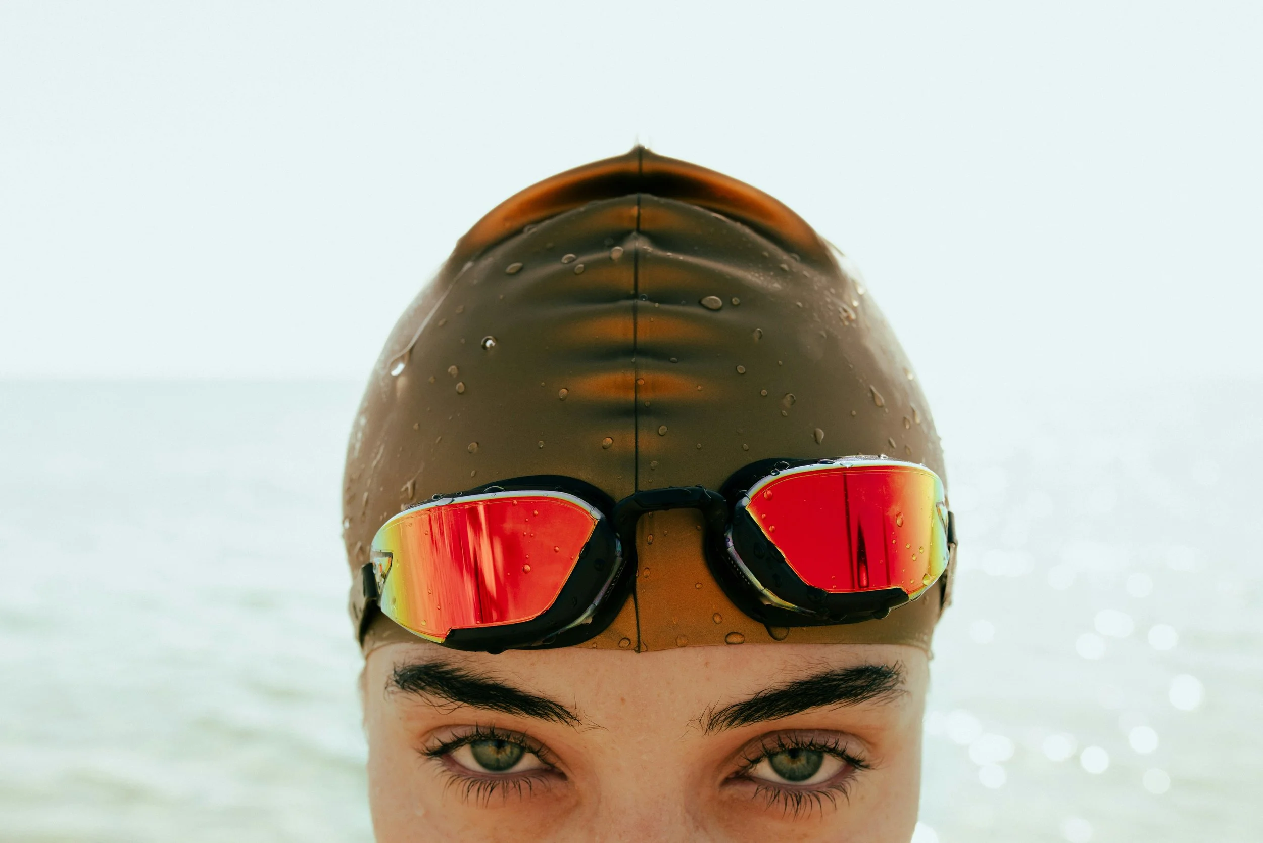 Close-up of swimmer in gold cap and red goggles looking towards camera