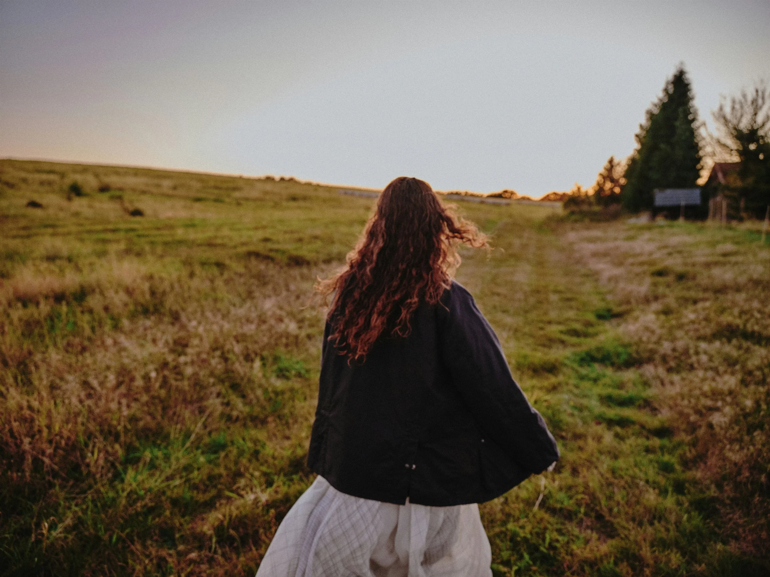 Woman walking across an open field at golden hour, symbolising natural movement and lifestyle-based longevity