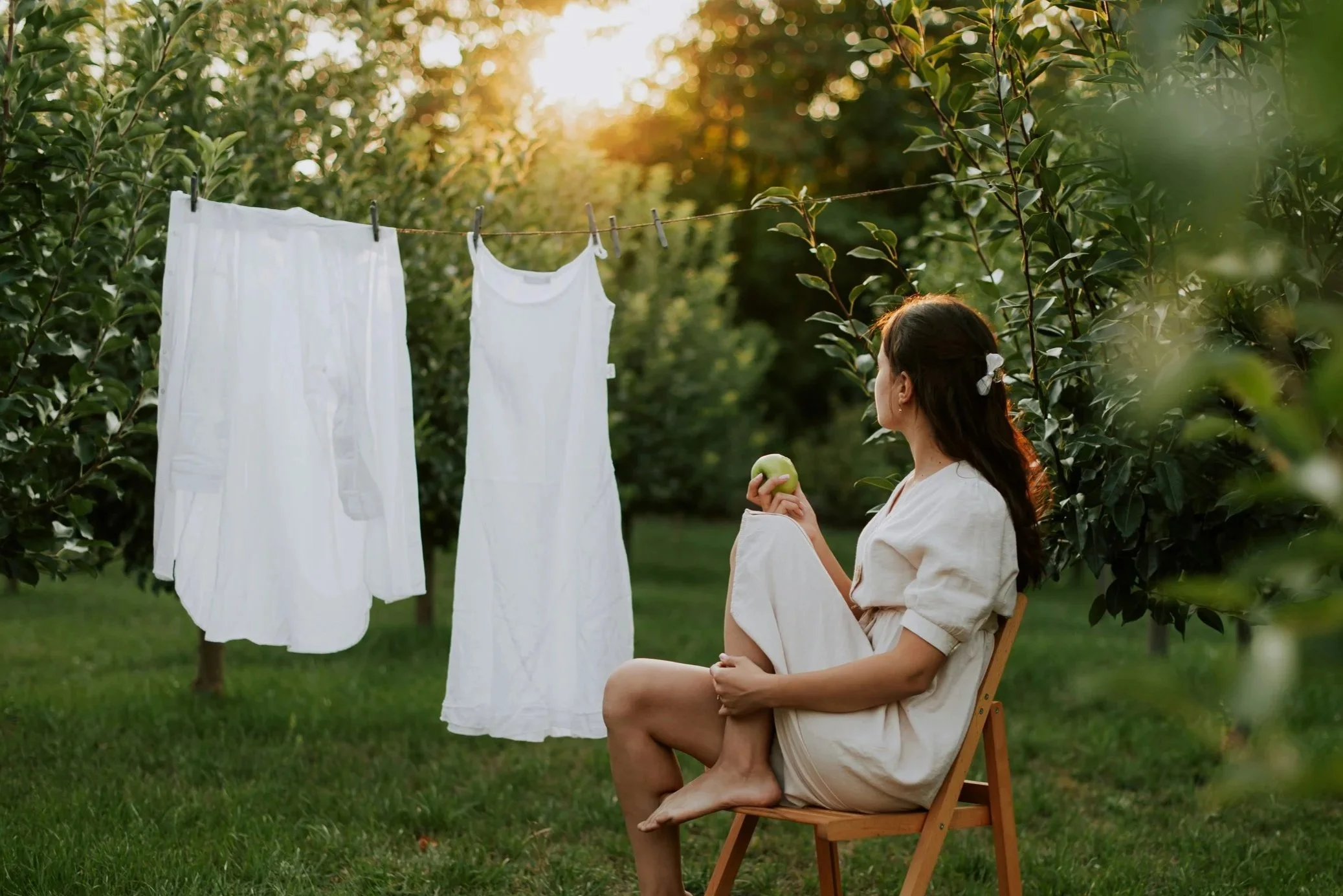 Woman sitting in a garden beside freshly washed white laundry drying on a clothesline, representing natural home cleaning and everyday laundry care.