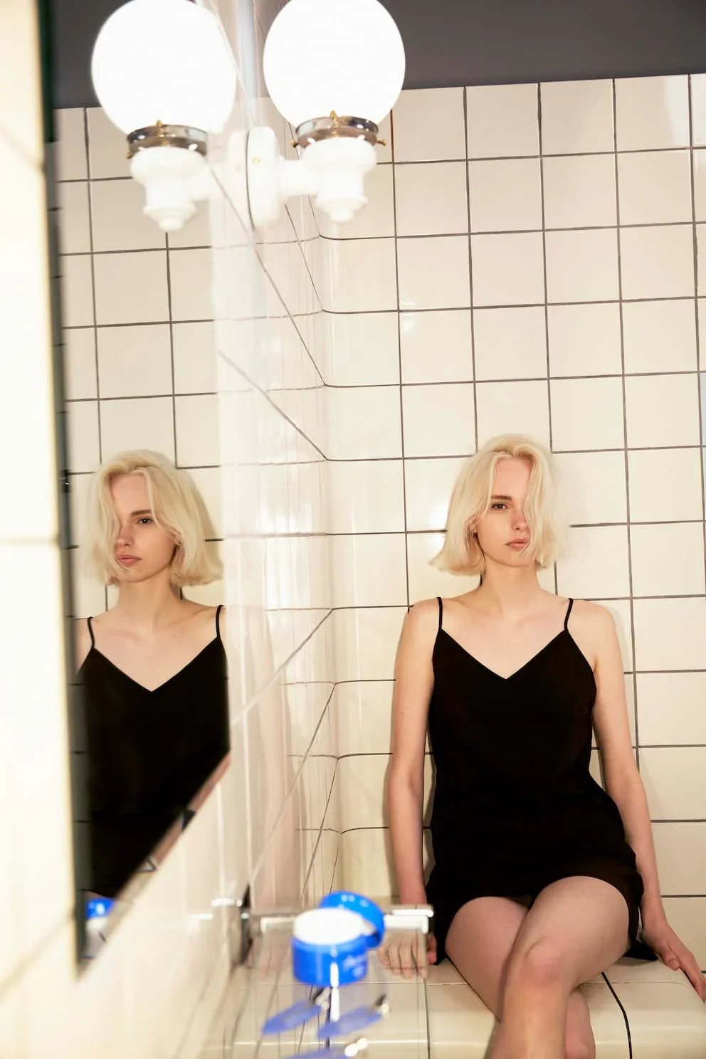 Woman with short, softly textured blonde hair sitting in a tiled bathroom, styled with natural movement and minimal heat for Hershesons campaign