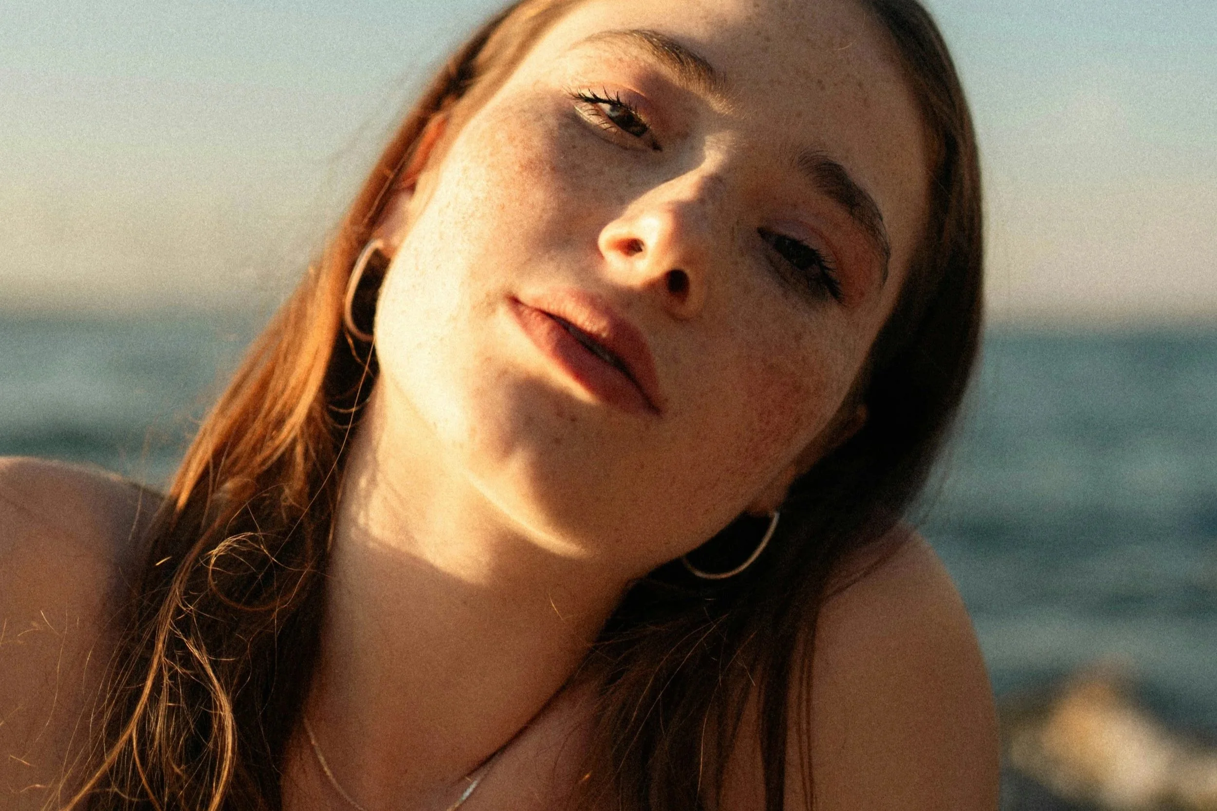 Woman with healthy, radiant skin outdoors by the sea, representing the French pharmacy skincare approach to ageing well.