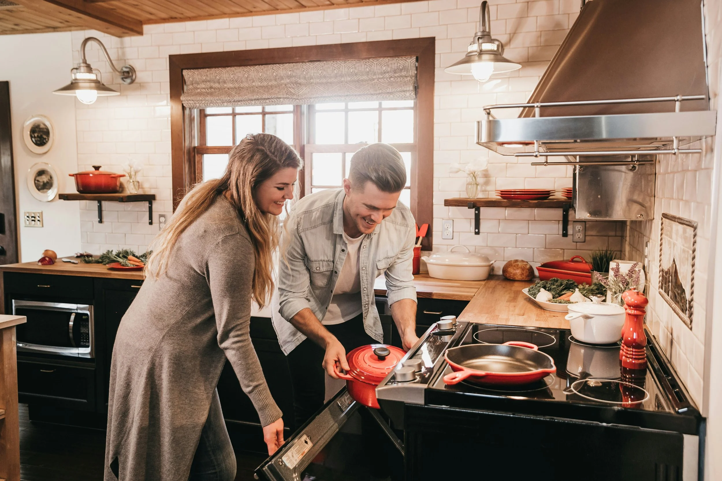 Couple cooking together in a bright modern kitchen with wooden countertops, white tiles and red cookware