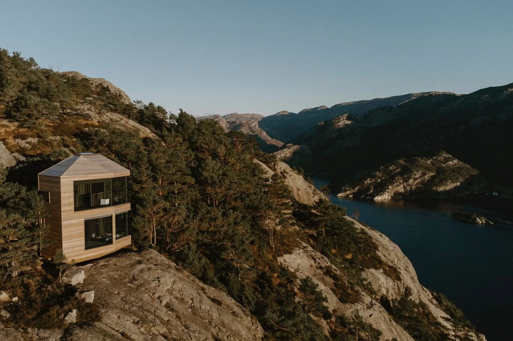 Floor-to-ceiling glass cabin overlooking autumn forest and rugged Norwegian mountains in Sunnmøre Alps at The Bolder Sky Lodges