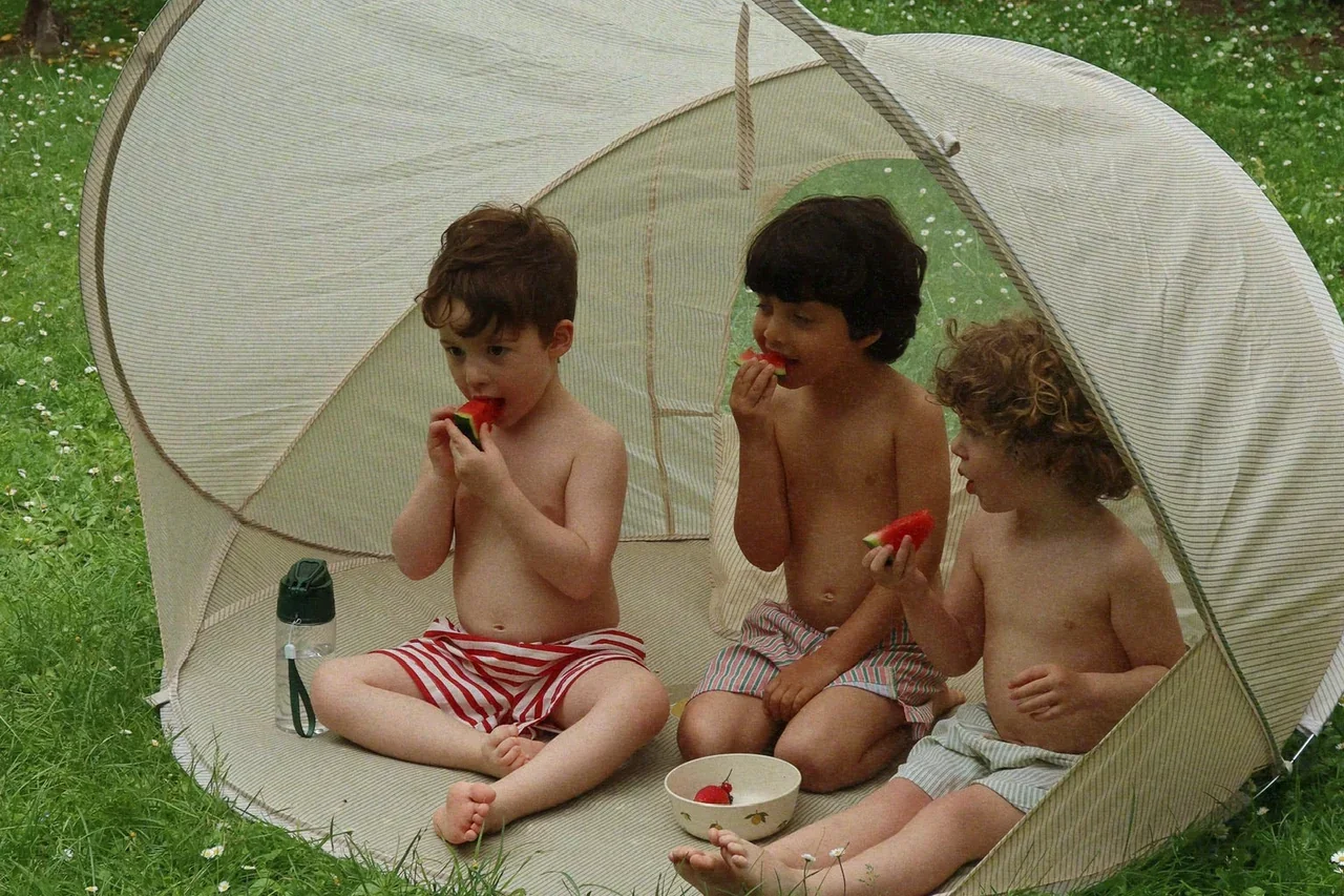 Children sitting inside a Konges Sløjd UPF 50+ pop-up sun tent enjoying watermelon on a hot summer's day.