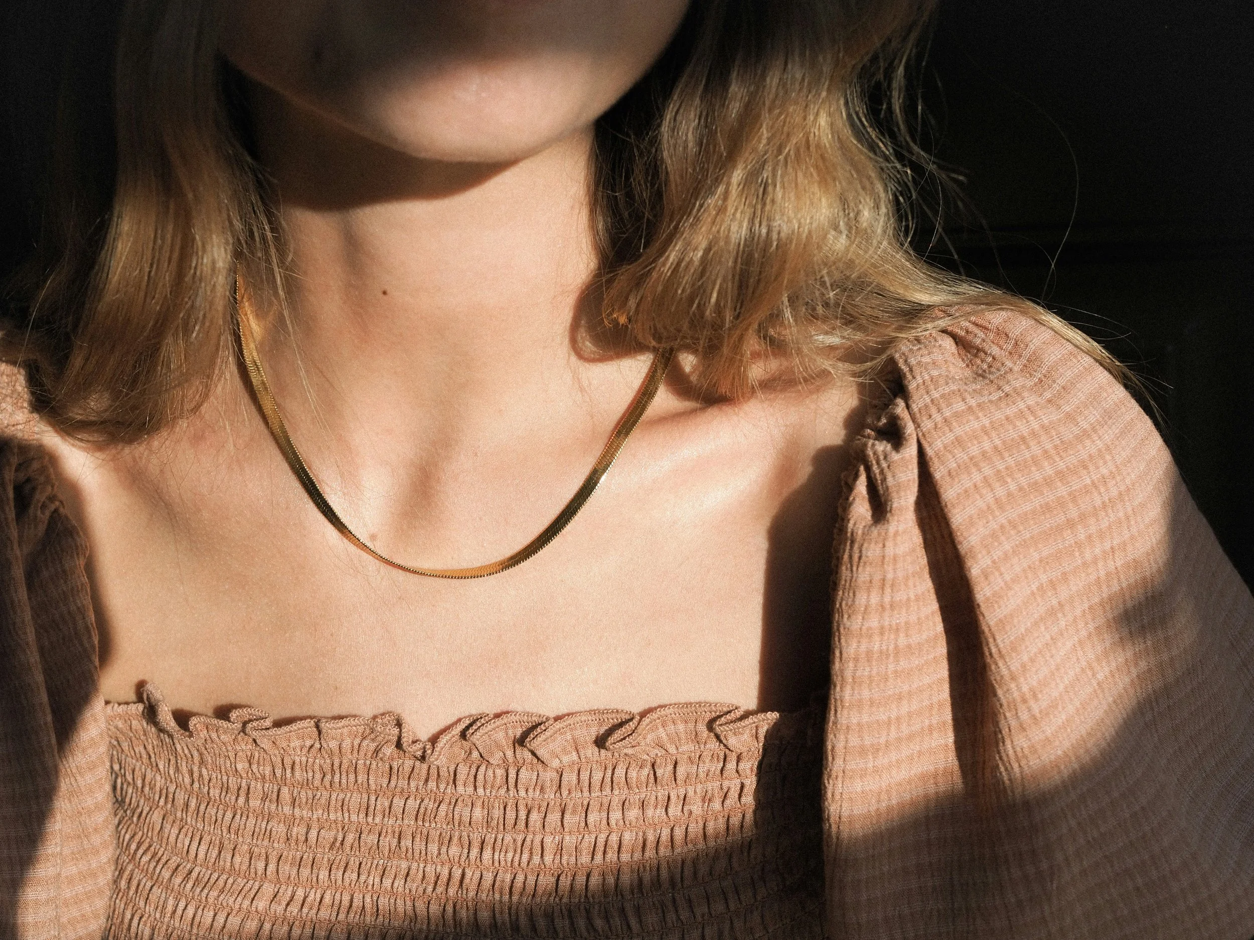 Woman wearing a simple gold chain necklace in warm sunlight