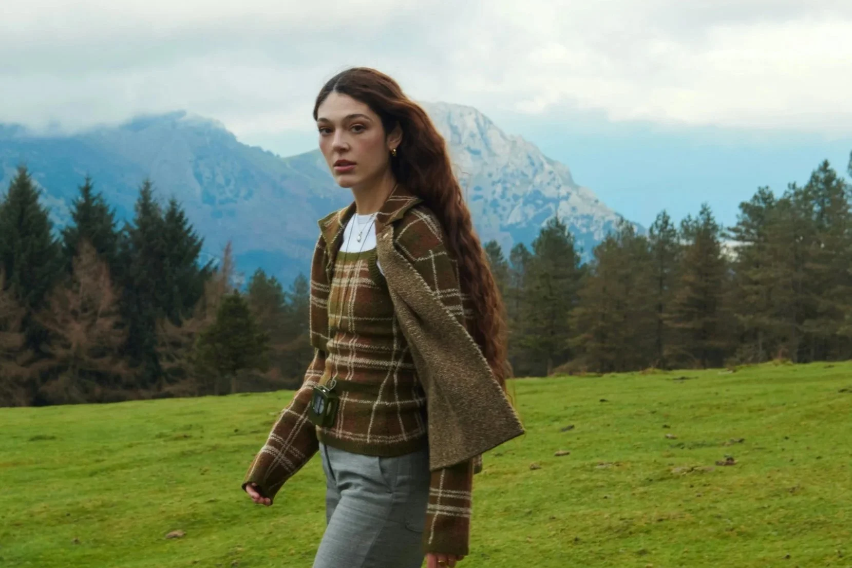 Woman with natural French-inspired makeup and glowing skin in an outdoor mountain setting.