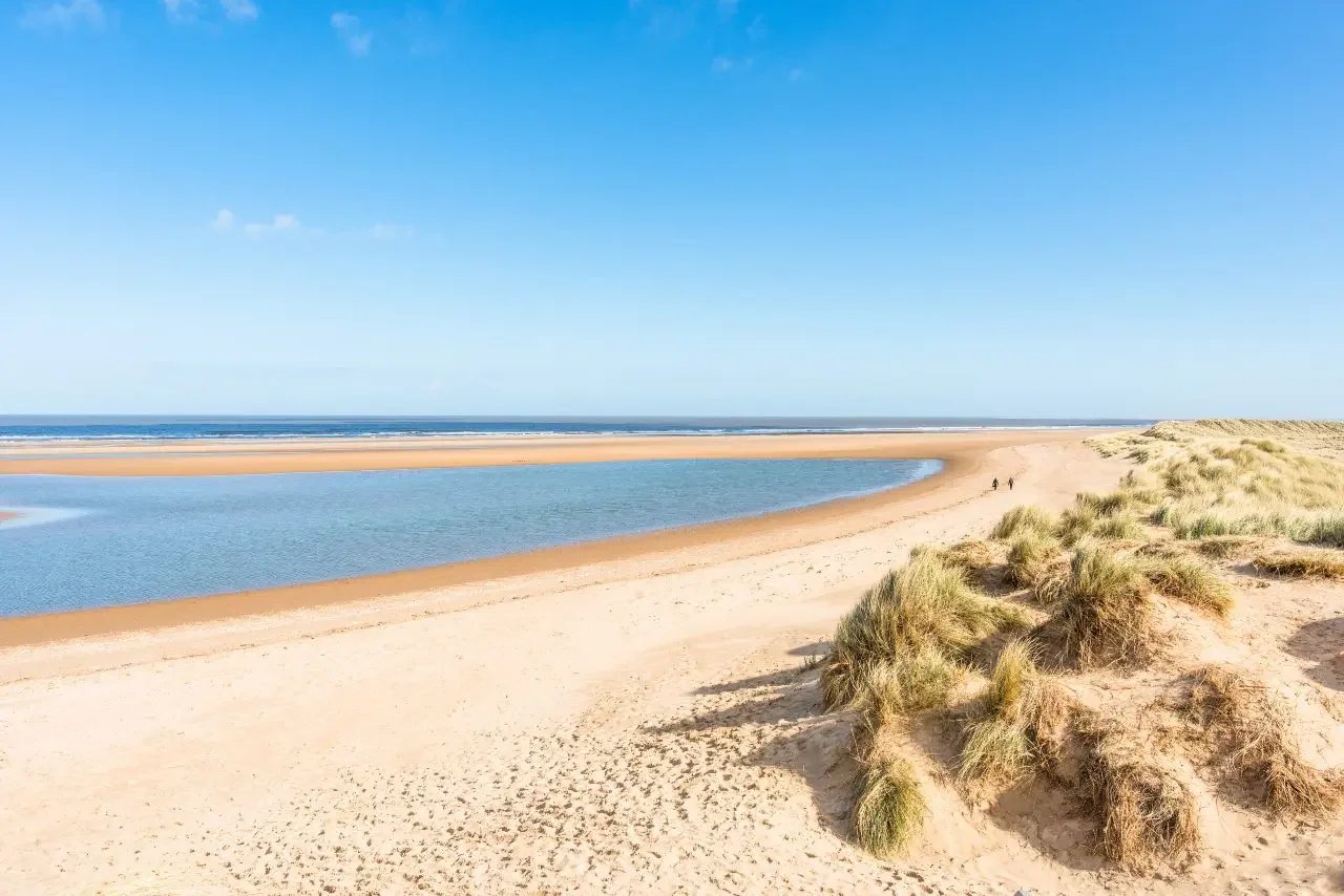 Holkham Beach in Norfolk with sweeping sand dunes, wide sandy shoreline and open coastal views.