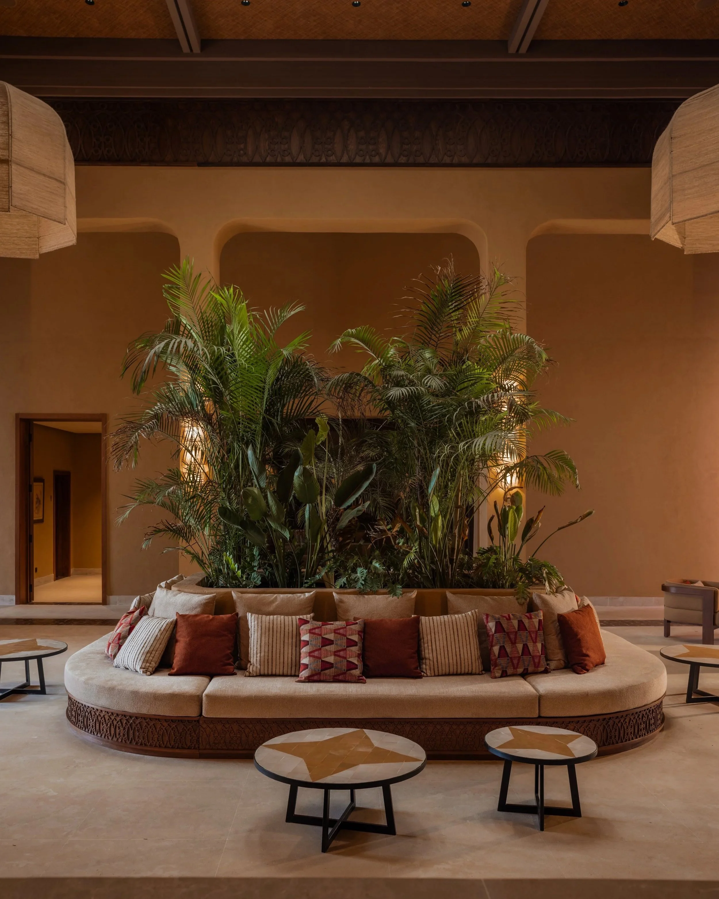 Curved cream sofa surrounding lush indoor planting in the contemporary lounge at Oasis Lodges Marrakech